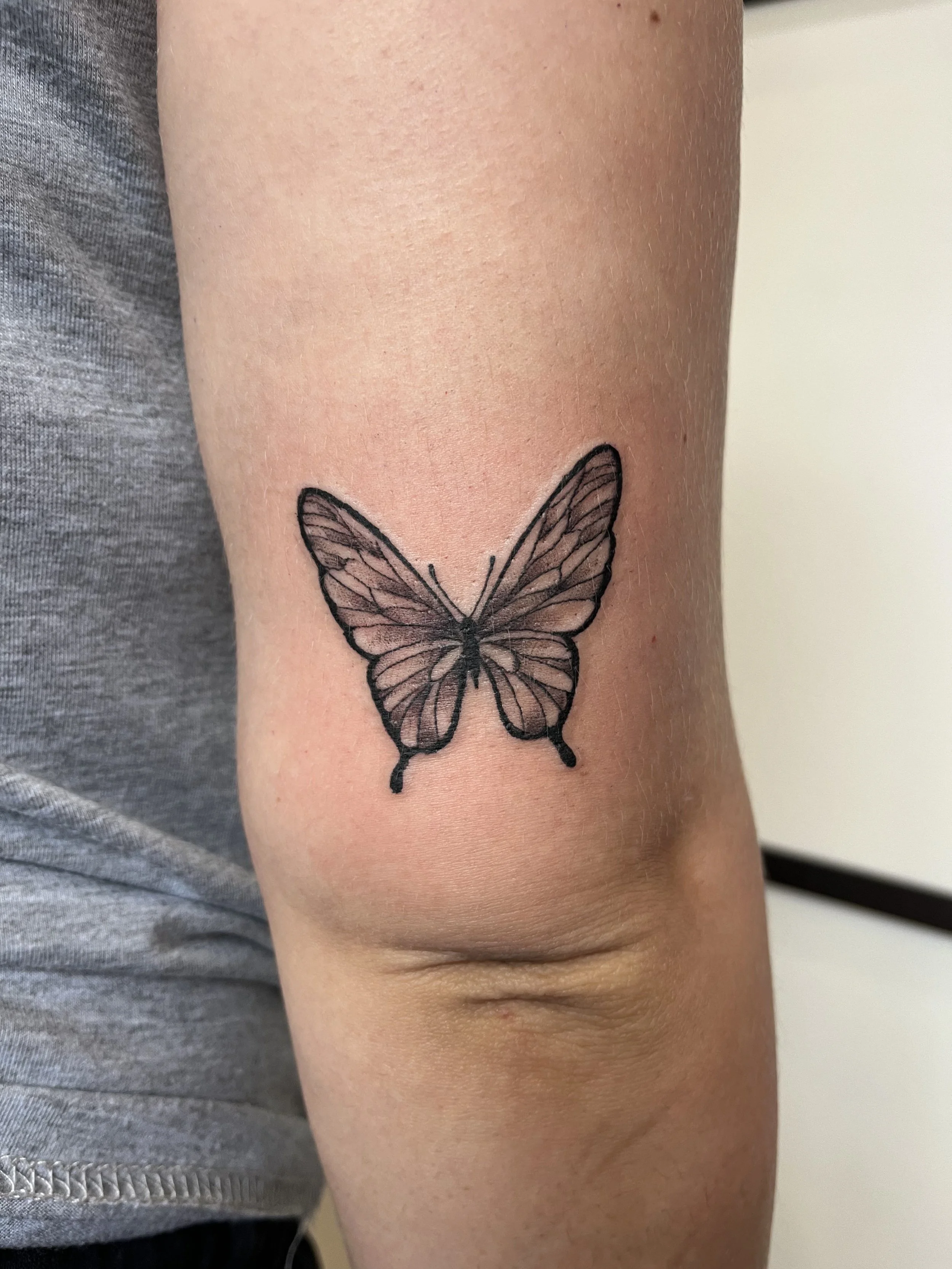 Tatouage blackwork représentant un papillon détaillé en noir et gris sur le bras.