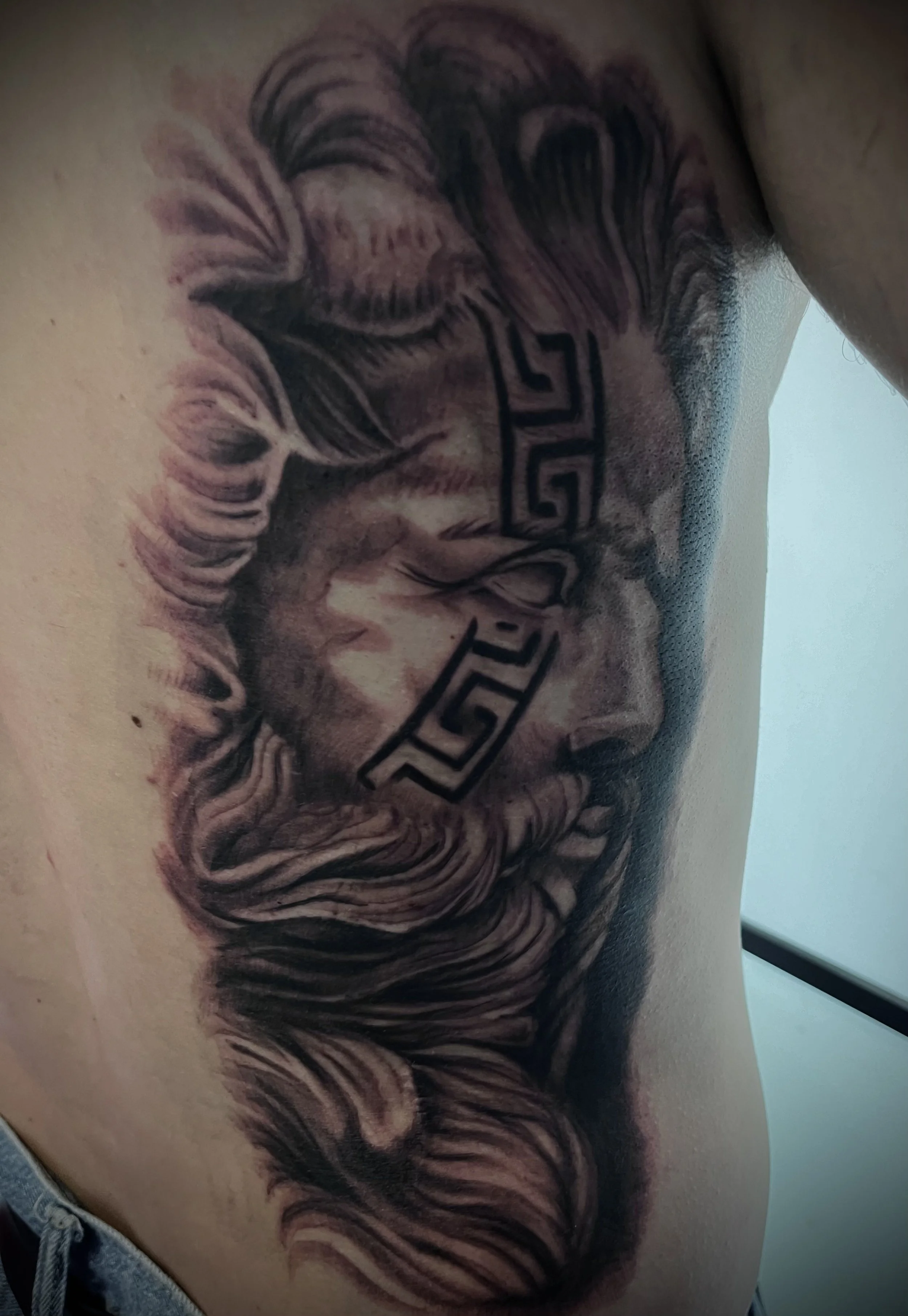 Tatouage blackwork représentant le dieu Zeus en portrait réaliste réalisé sur les côtes.