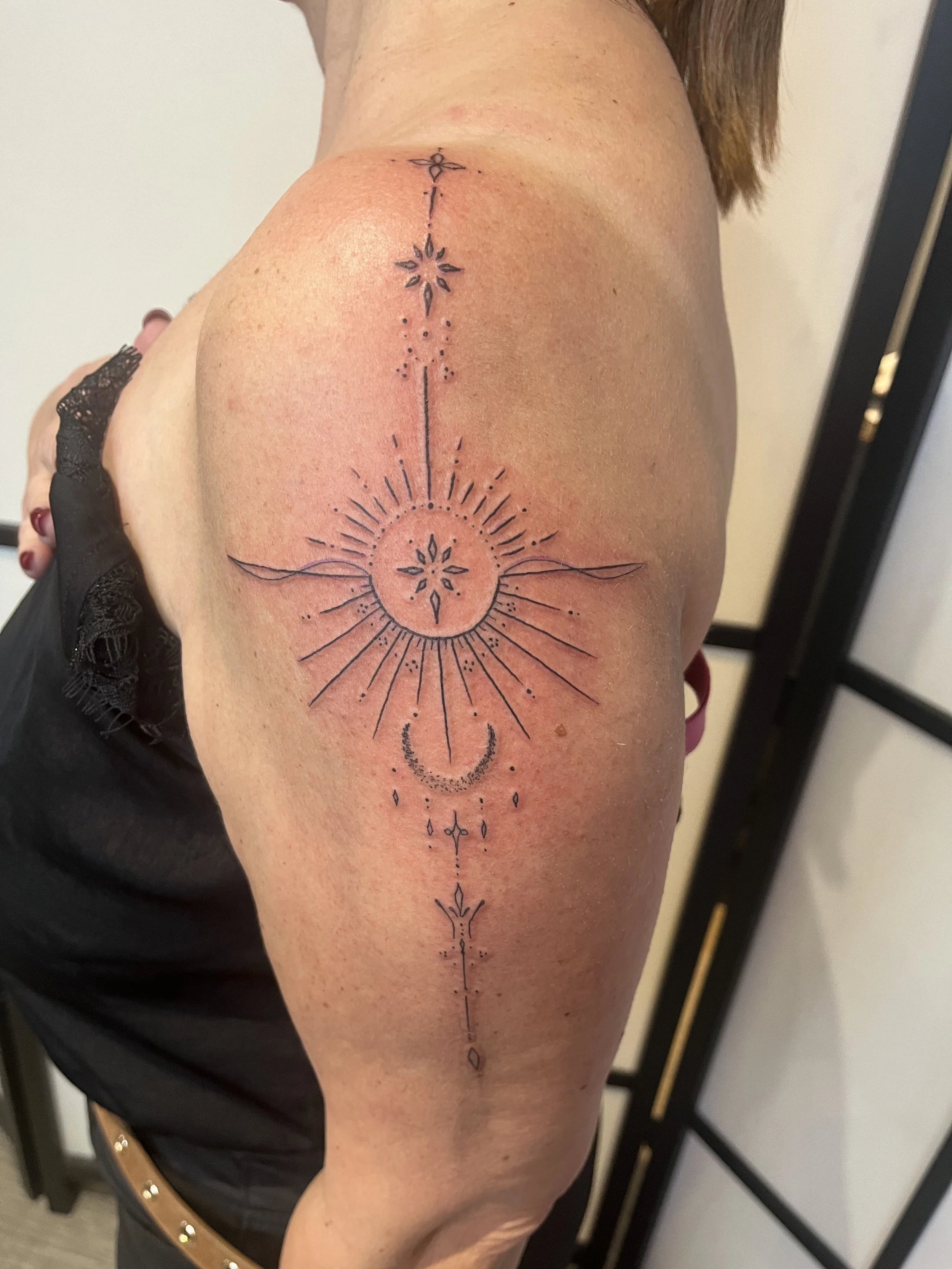 Tatouage ornemental en lignes fines représentant un motif céleste et géométrique sur le bras.
