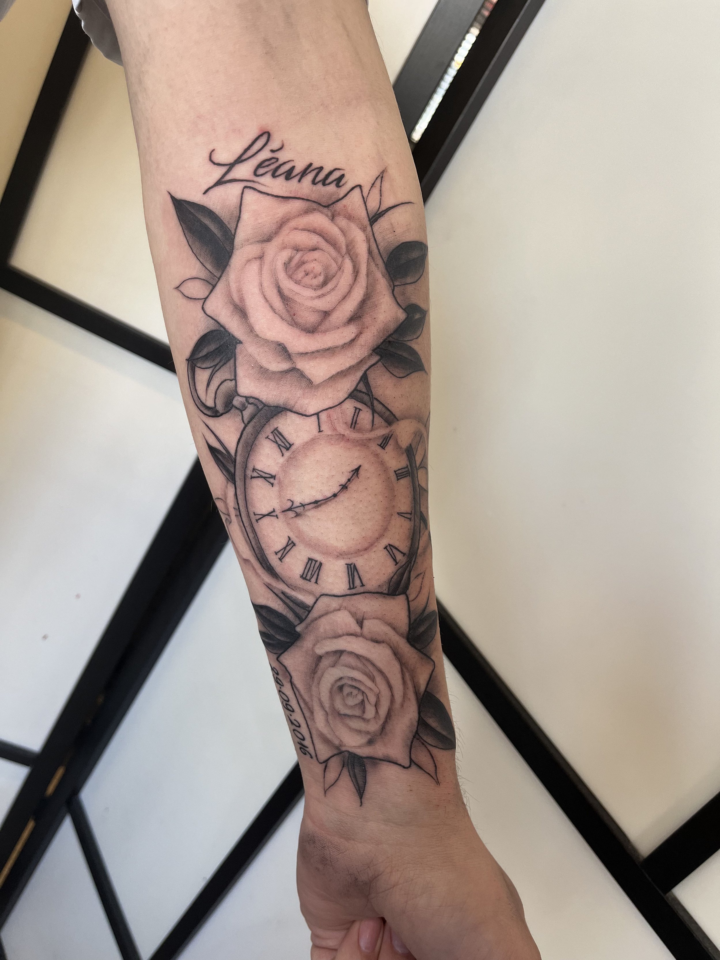 Tatouage réaliste représentant des roses accompagnées d’une horloge à chiffres romains sur le bras.