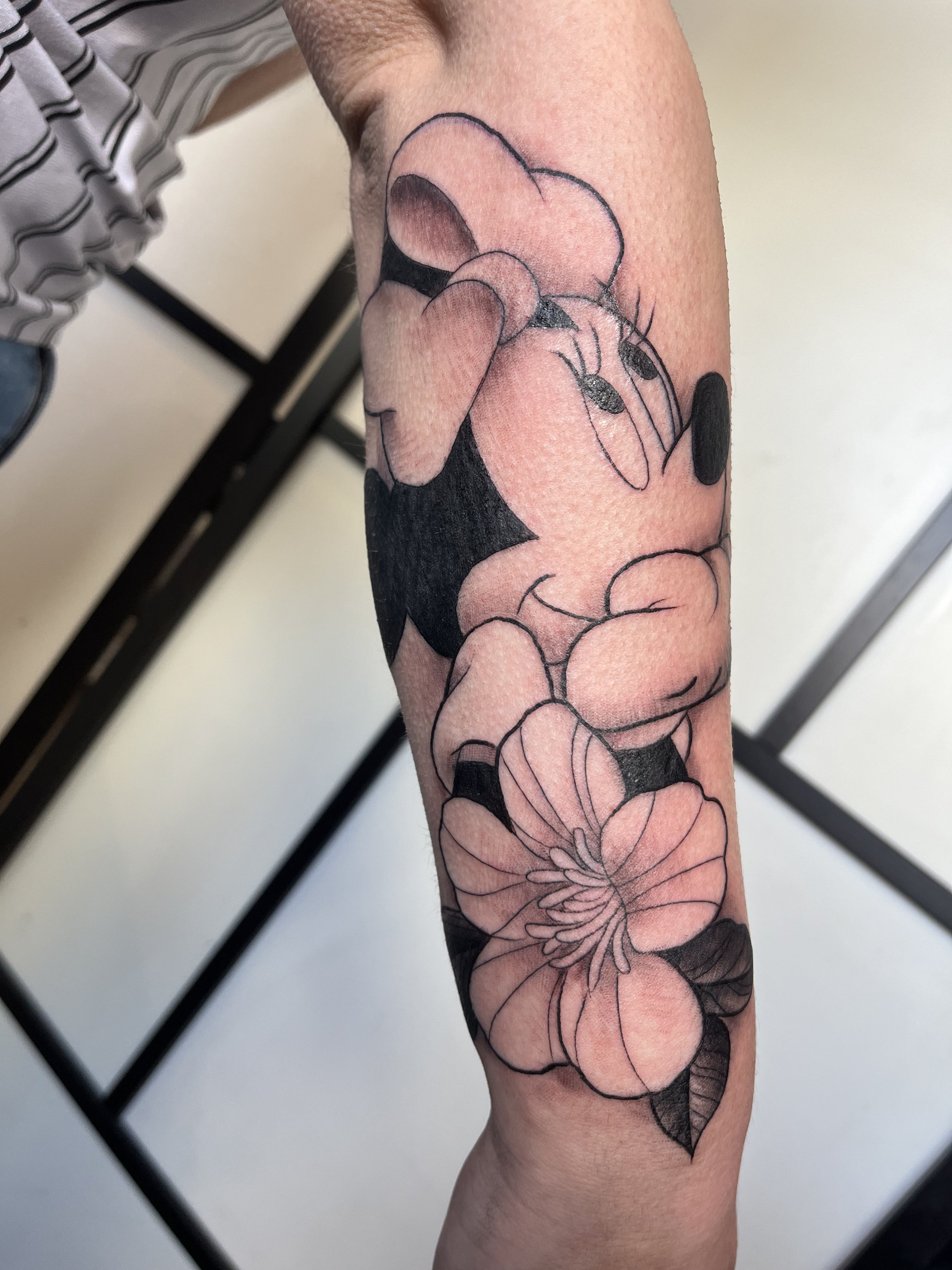 Tatouage cartoon représentant Minnie Mouse accompagnée de fleurs sur le bras.