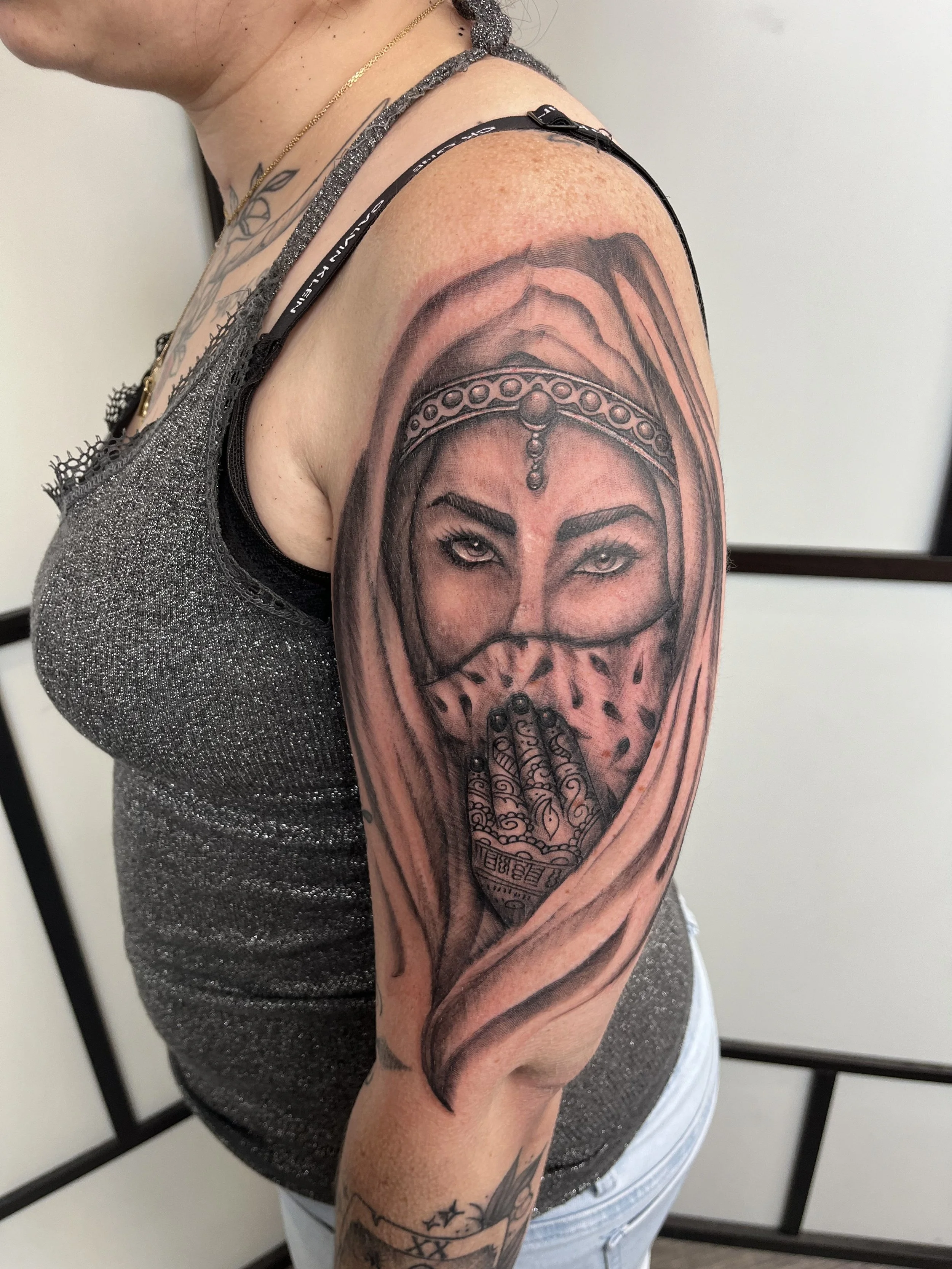 Tatouage réaliste représentant un visage oriental voilé avec détails ornementaux sur le bras.