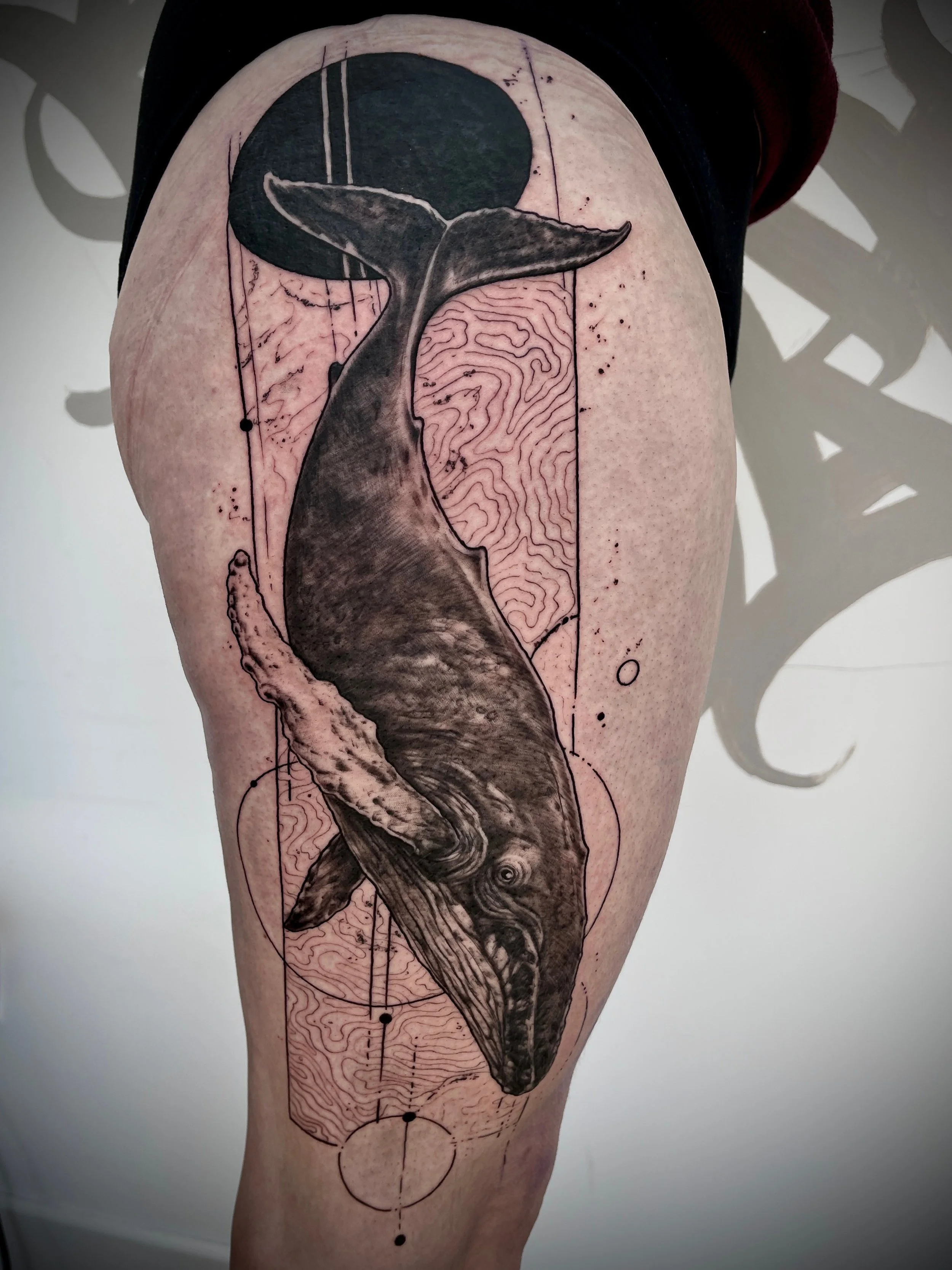 Tatouage réaliste et géométrique représentant une baleine avec éléments graphiques sur la jambe.