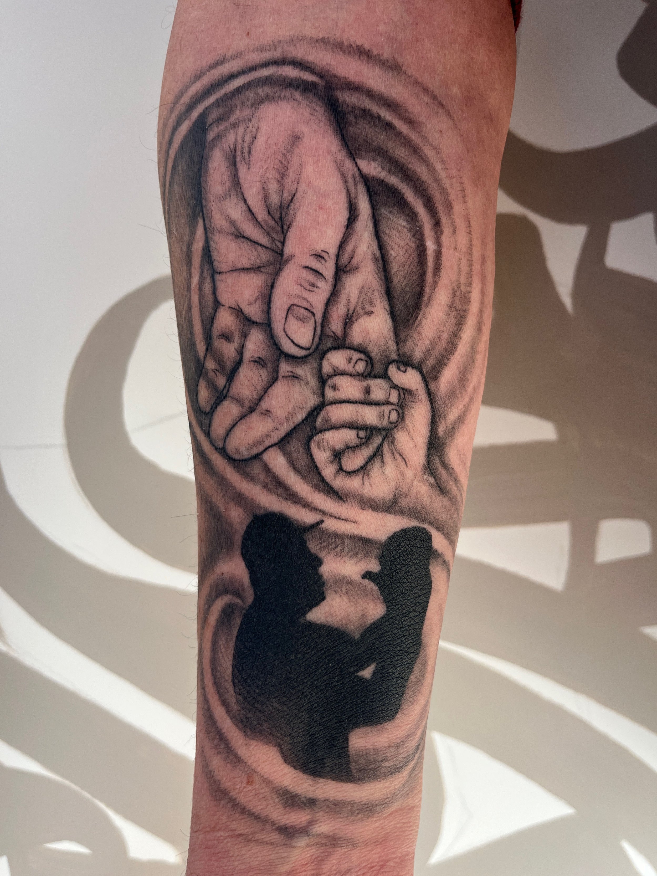 Tatouage blackwork représentant une main d’adulte tenant la main d’un enfant avec silhouette père et fille sur le bras.