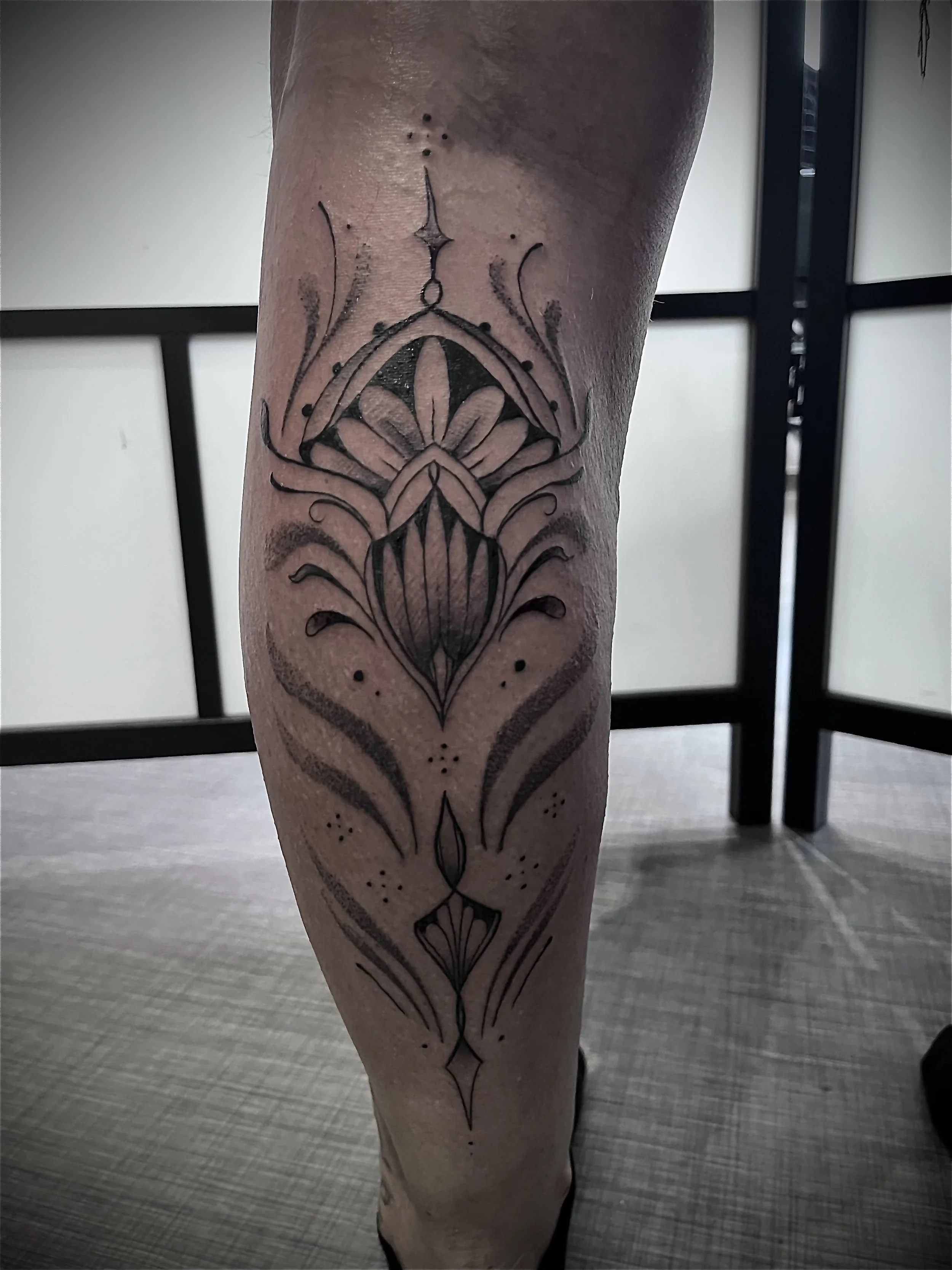 Tatouage ornemental géométrique réalisé en lignes fines sur la jambe.