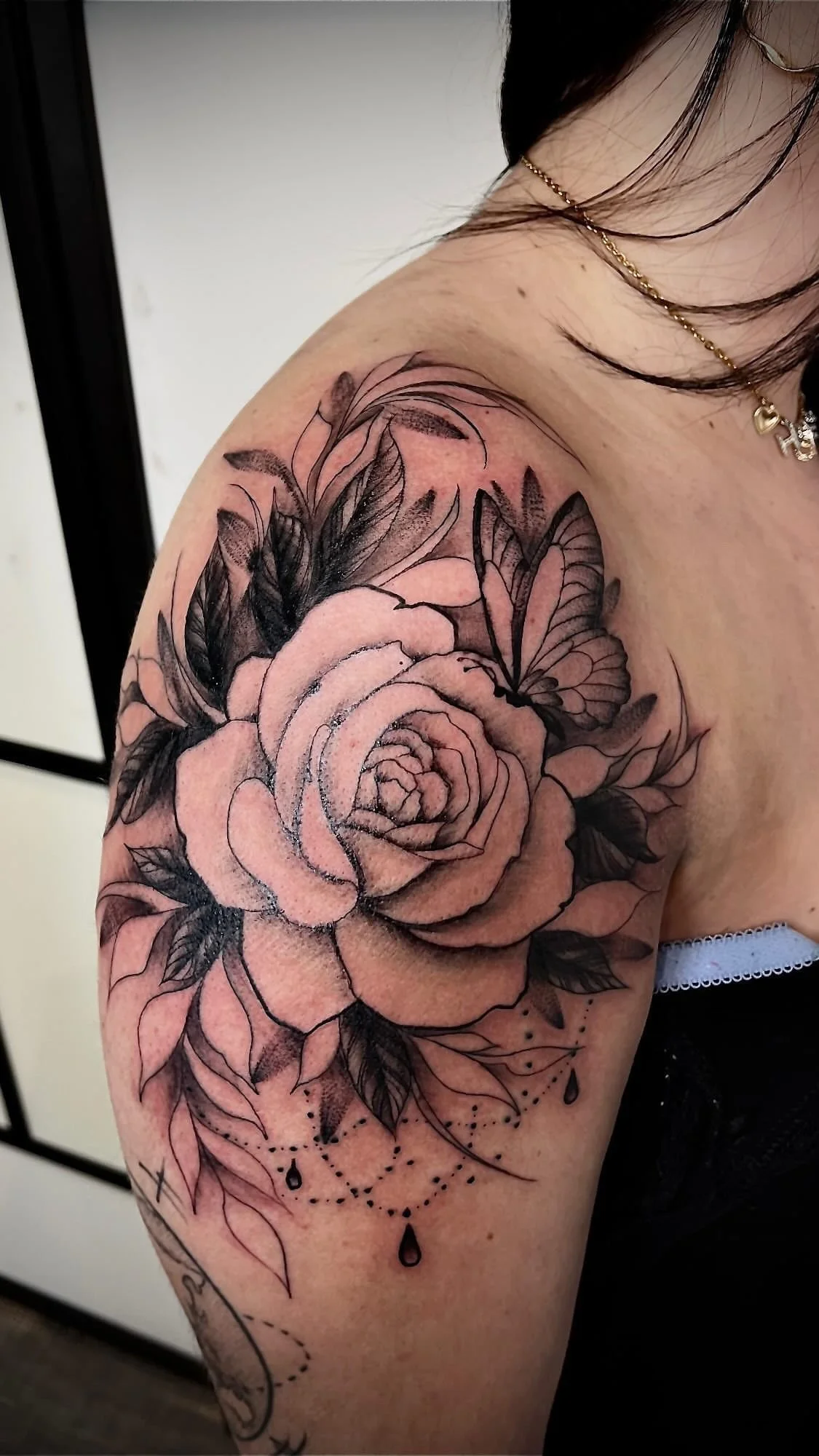 Tatouage blackwork représentant une rose florale accompagnée de papillons sur le bras.