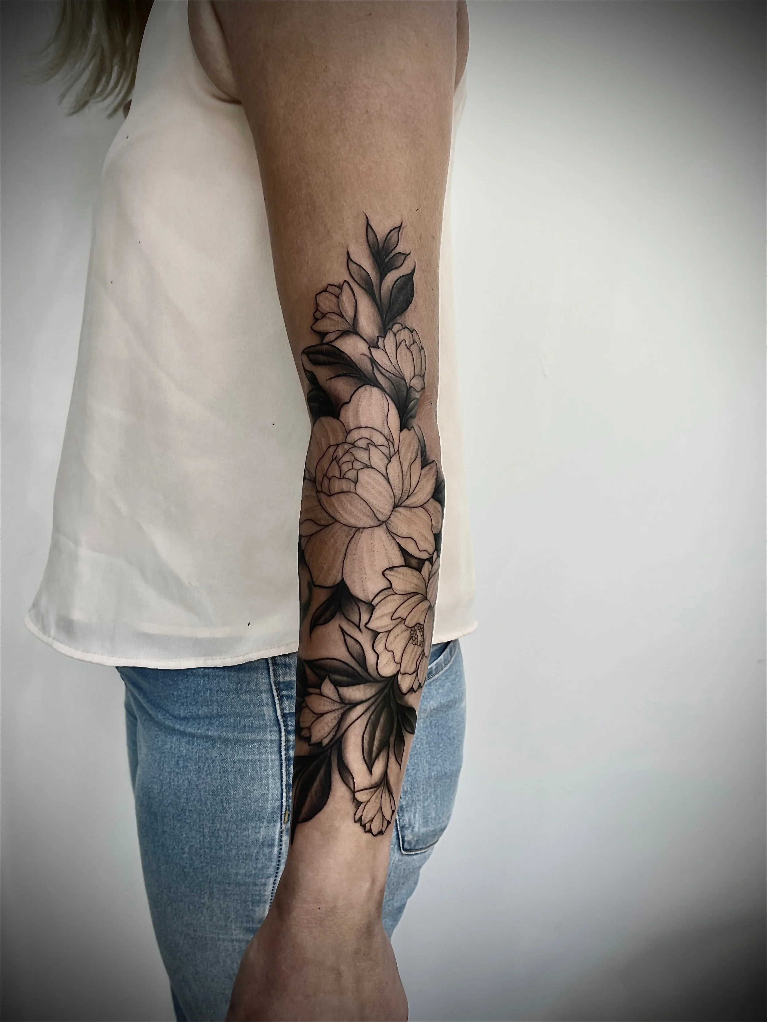 Tatouage réaliste de pivoines florales en noir et gris réalisé sur le bras.