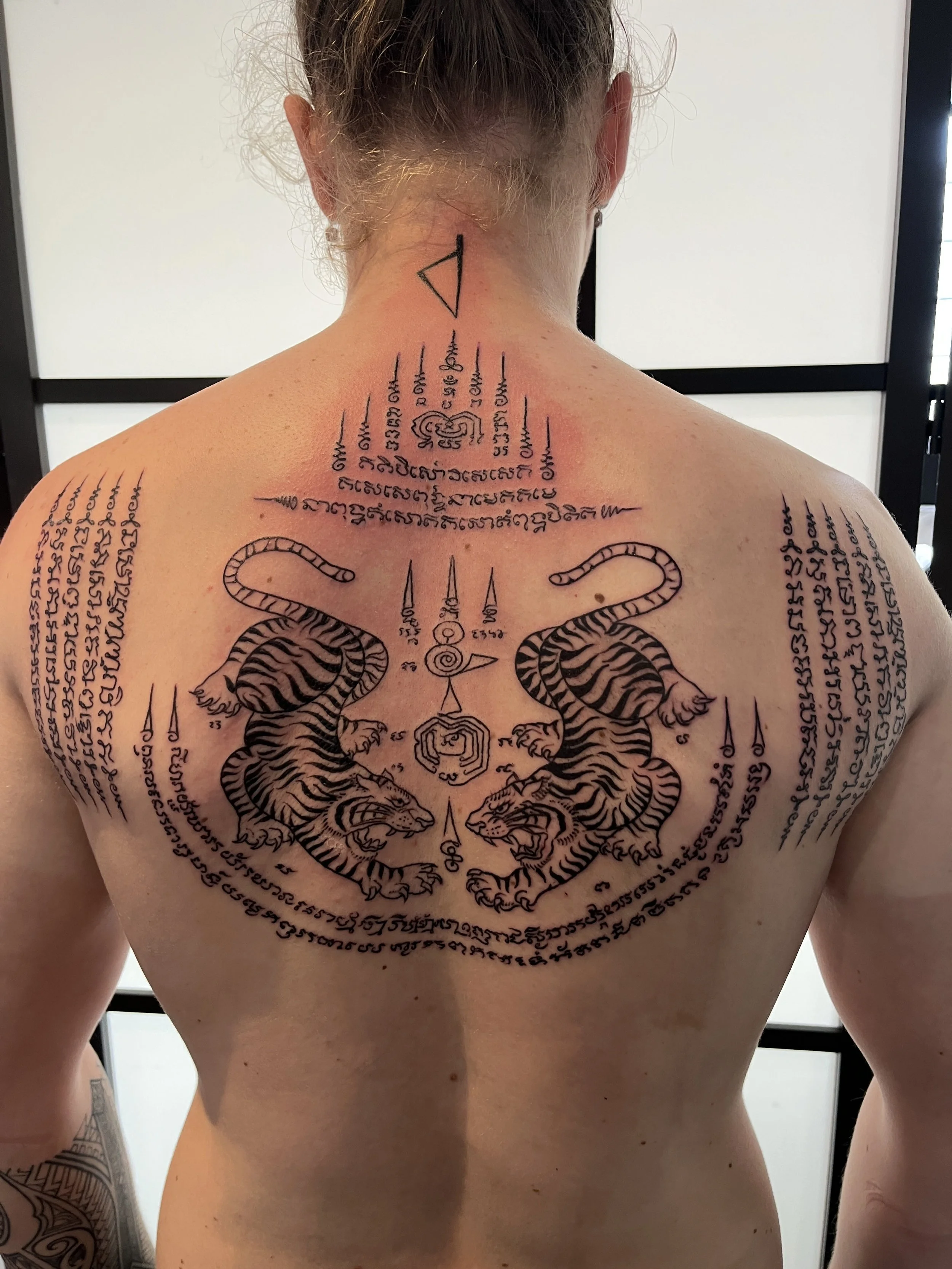 Tatouage thaï sacré dans le dos avec deux tigres symétriques et écritures spirituelles traditionnelles.