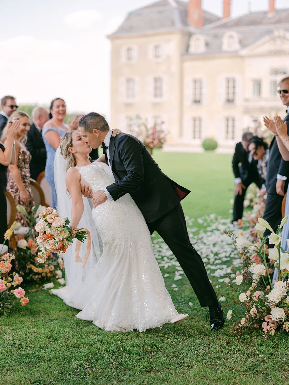 Bride and groom kiss during outdoor wedding ceremony surrounded by guests