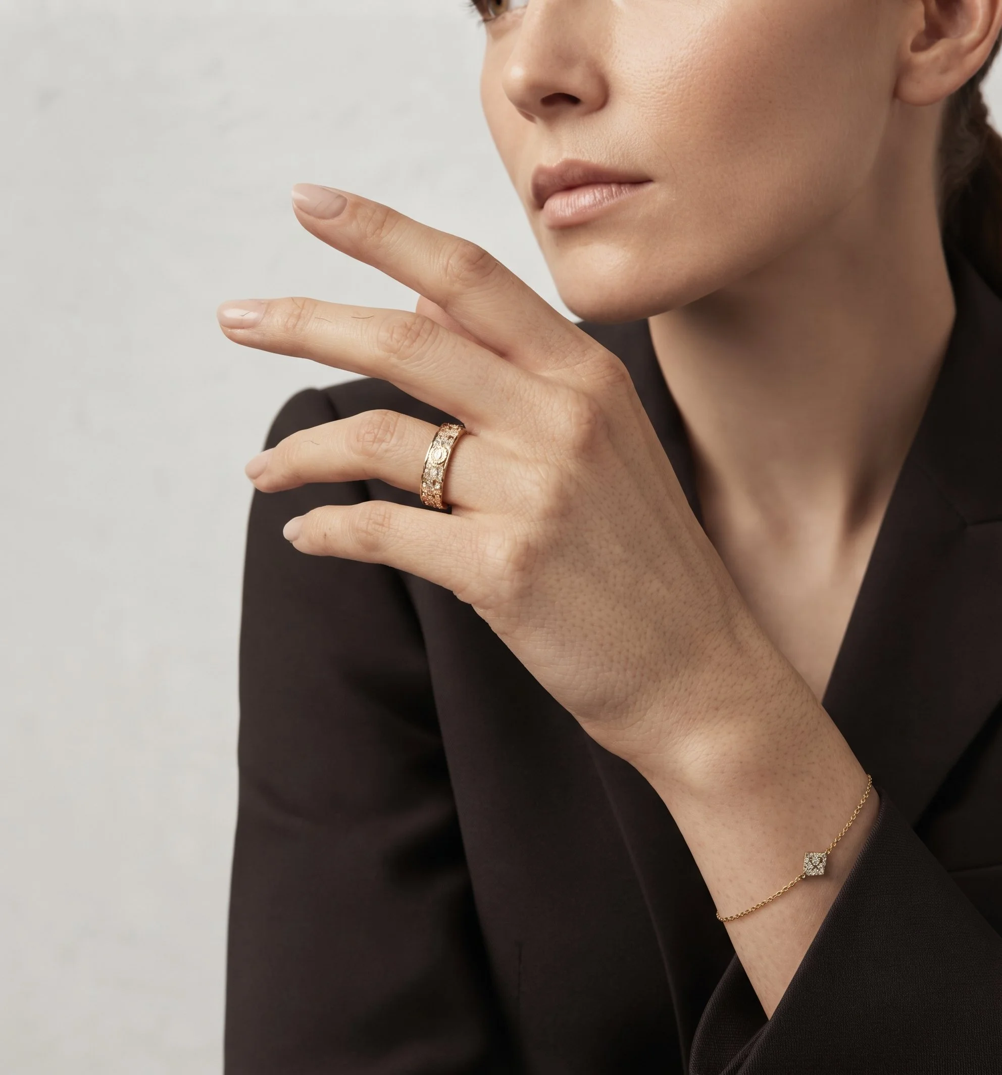 Femme en veste noire, main près du visage, bague et bracelet fins en or, portrait joaillerie généré par IA