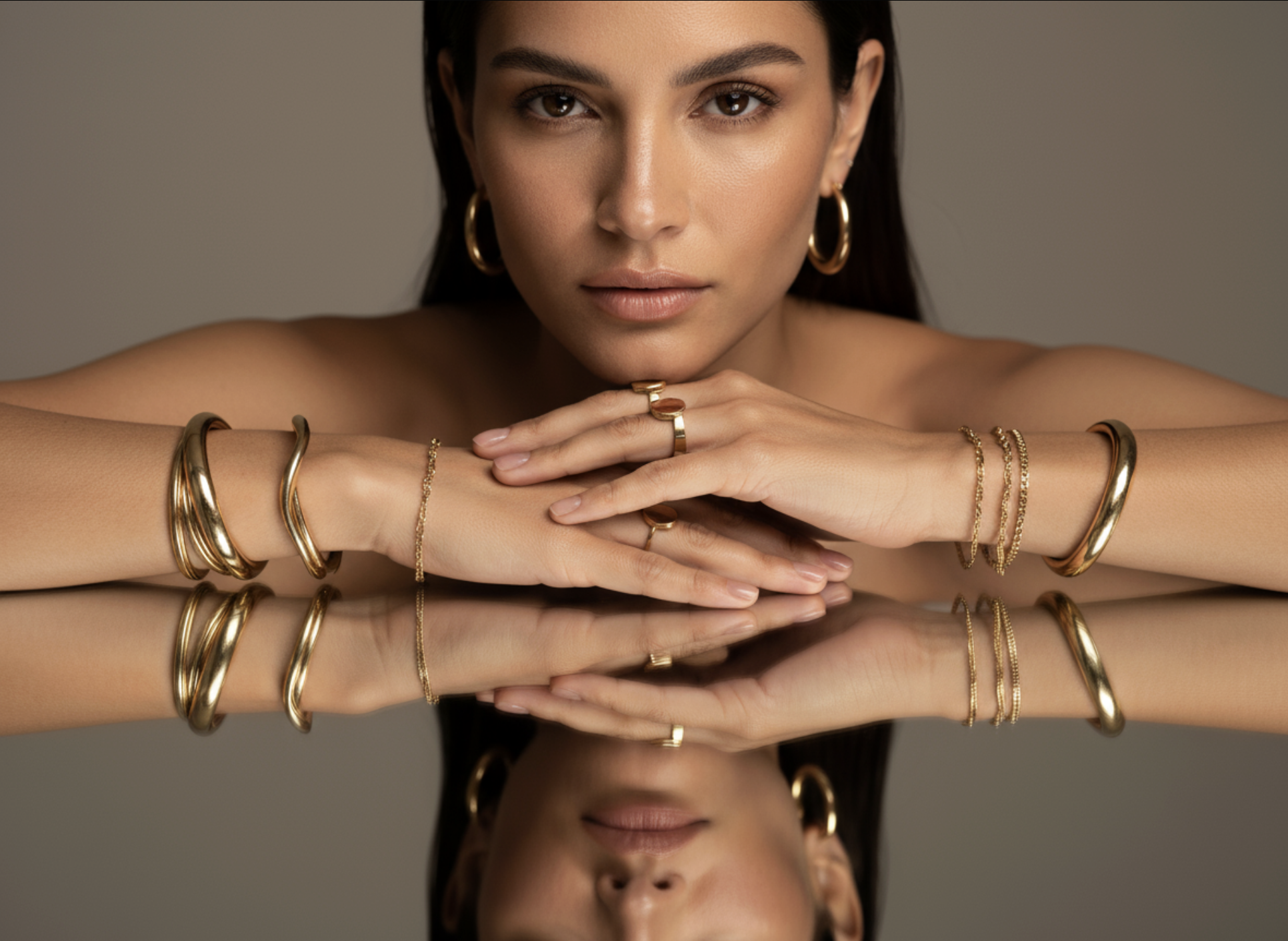 Femme brune accoudée, mains couvertes de bijoux en or se reflétant sur une surface miroir, campagne joaillerie IA