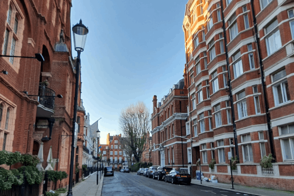 A street lined with red brick buildings and parked cars under a clear blue sky.