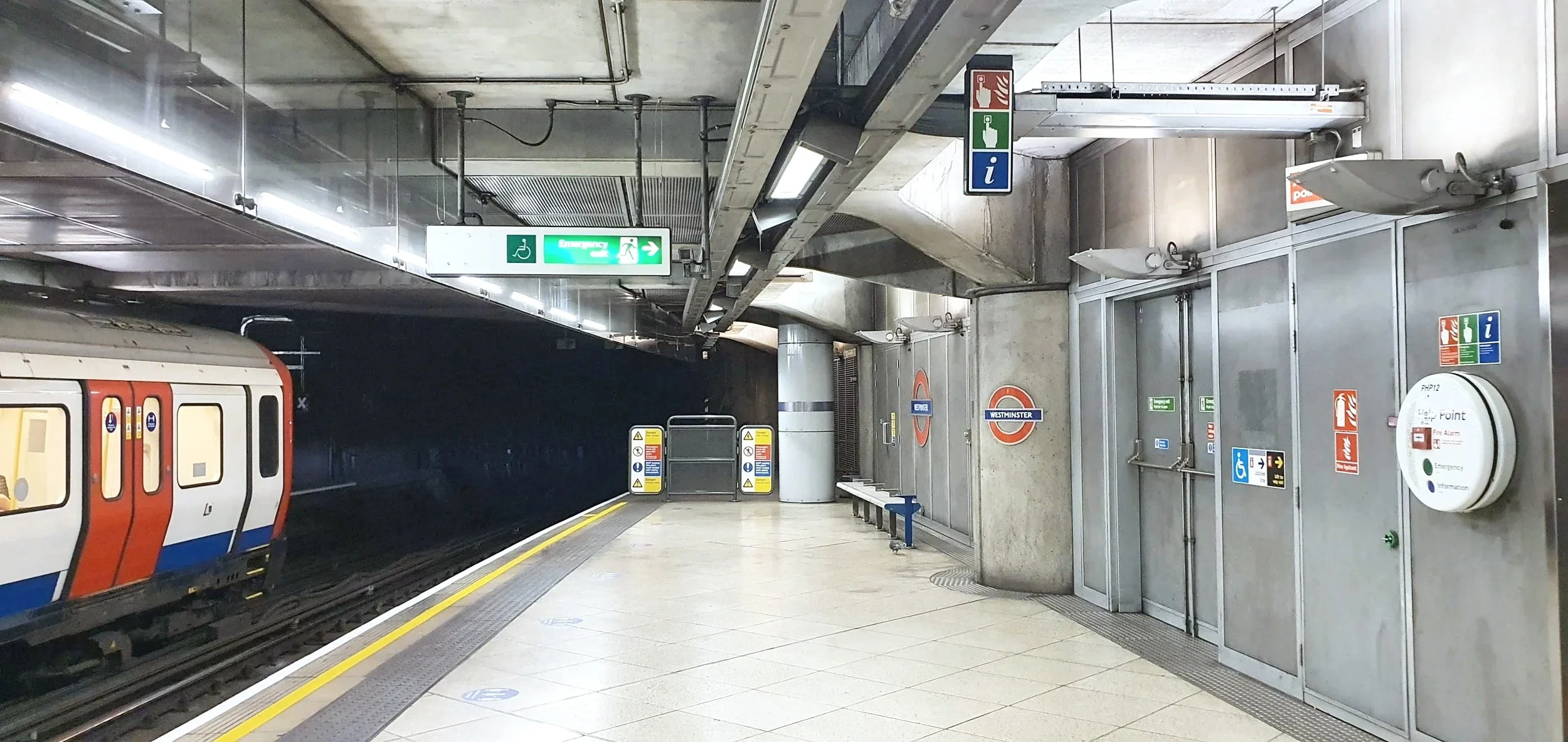 Two construction workers, one in a white helmet and the other in an orange helmet, reviewing plans in a train maintenance facility while a modern red and white train is on the tracks nearby.