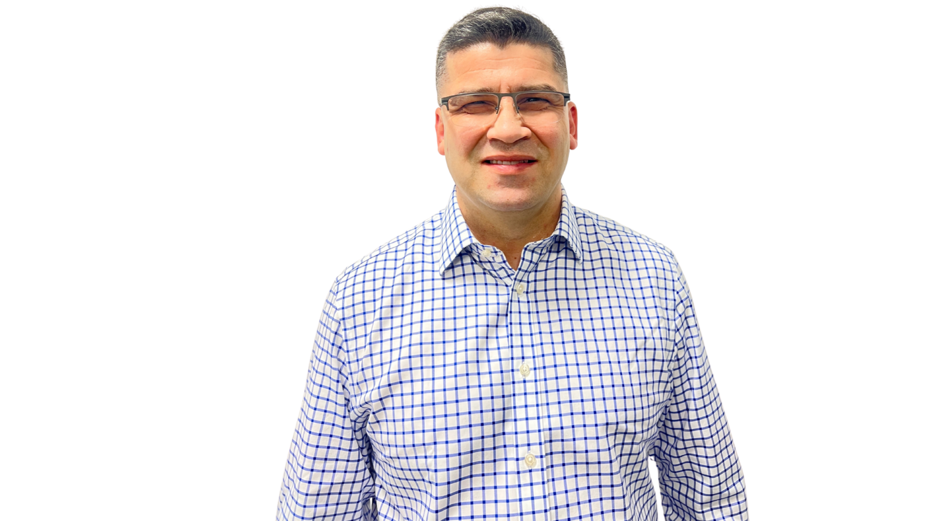 A man with short dark hair and glasses wearing a blue and white checkered shirt, standing outdoors against a black background with colored horizontal bars.