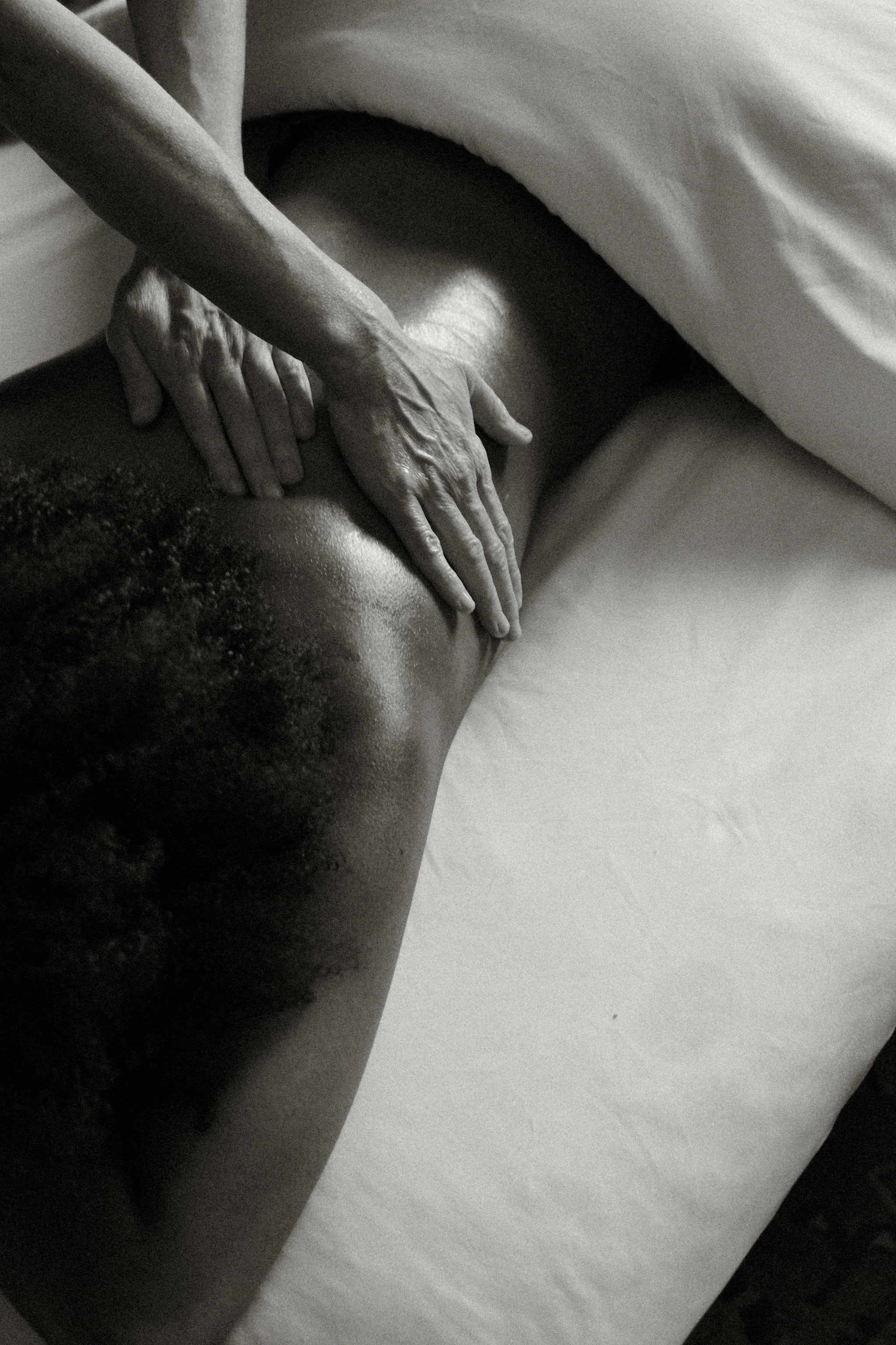 Black and white photo of a person receiving a back massage, with hands positioned on their upper back and shoulders, on a massage table.