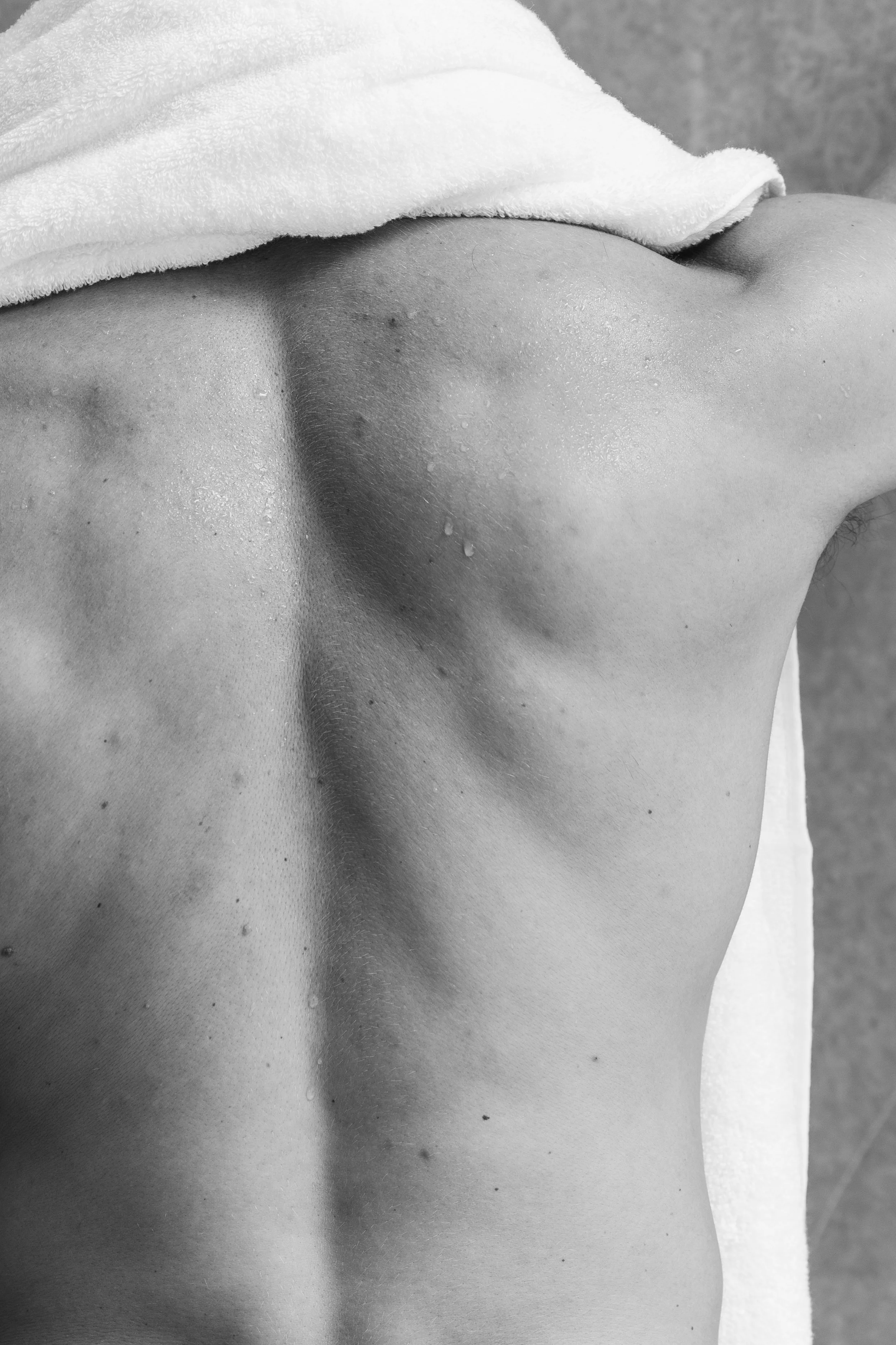 Close-up of a person's upper back and shoulder, with a towel draped over the shoulder and water droplets on the skin.