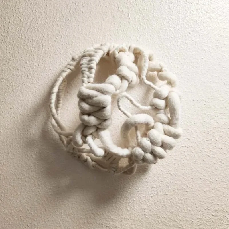 Abstract white textile art sculpture mounted on a wall.