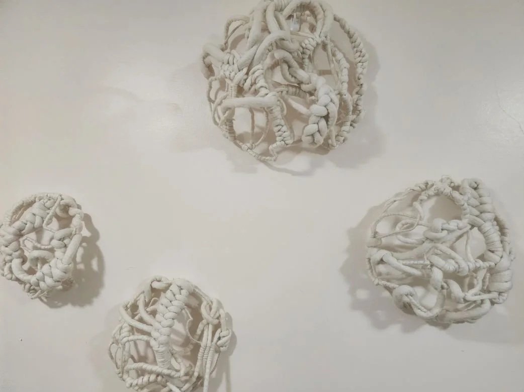 Four white abstract art sculptures made of knotted and intertwined fabric or material, arranged on a white surface.
