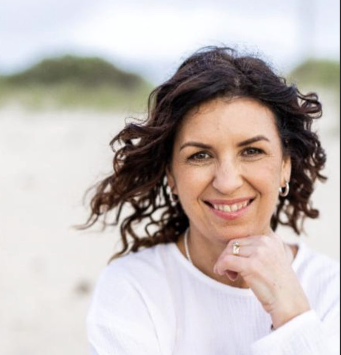 Close-up of a woman with curly brown hair smiling on a beach