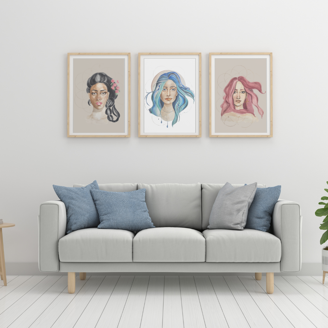 Three framed portraits of women with different hairstyles and colors hanging above a white sofa with blue and gray pillows, in a minimalistic living room with white walls and wooden flooring.