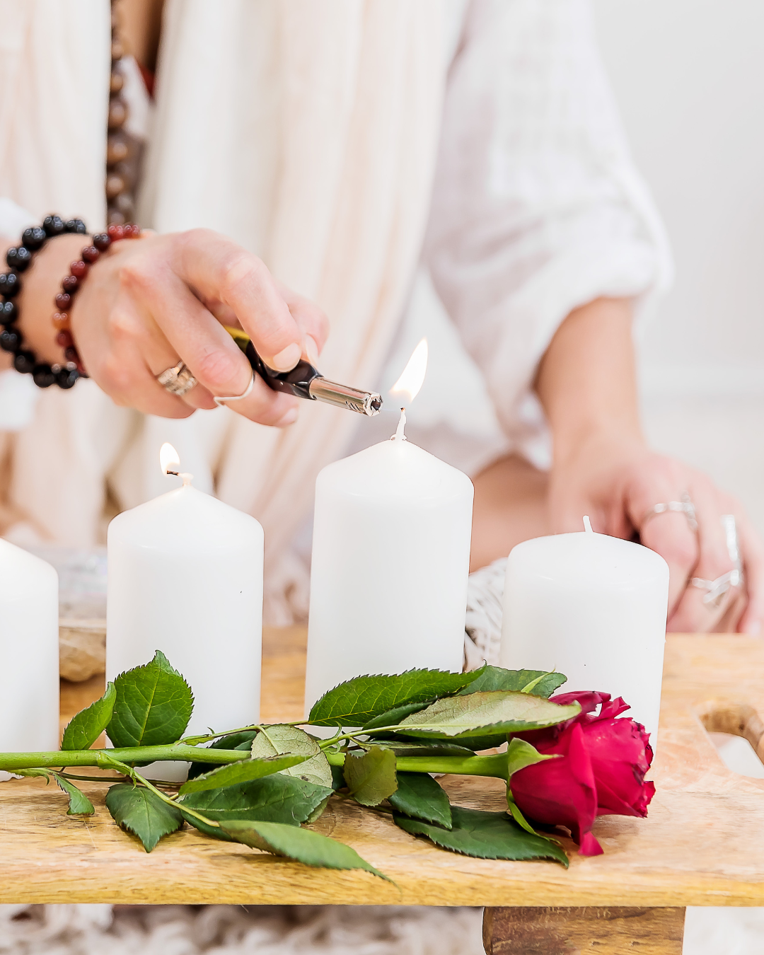 woman's hand lighting a white candle in ceremony with rose on table