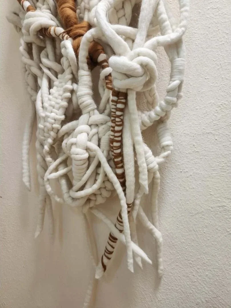A piece of wall art made from thick, intertwined white and brown striped yarns or ropes hanging on a wall.