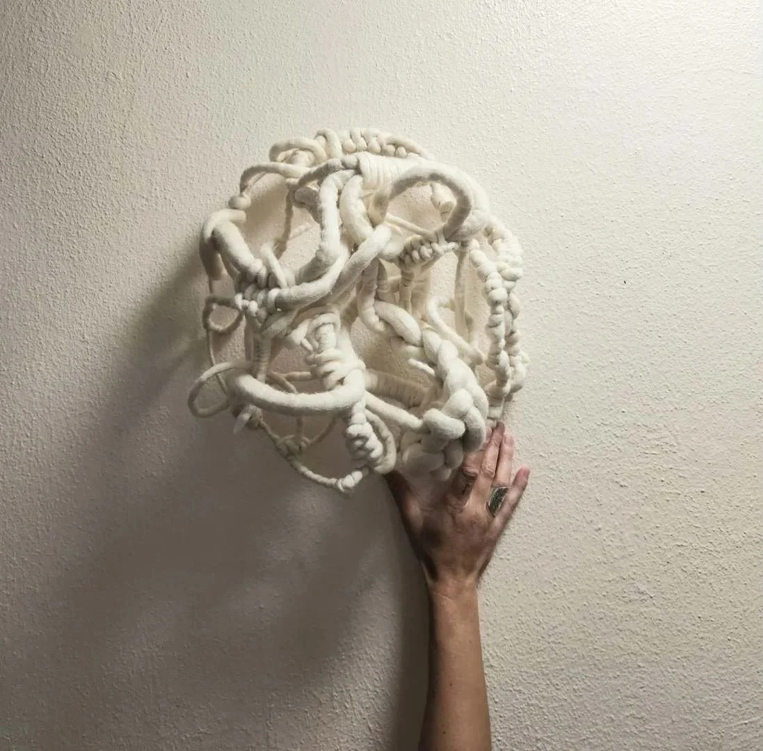 hand gently holding a round structured white textile artwork
