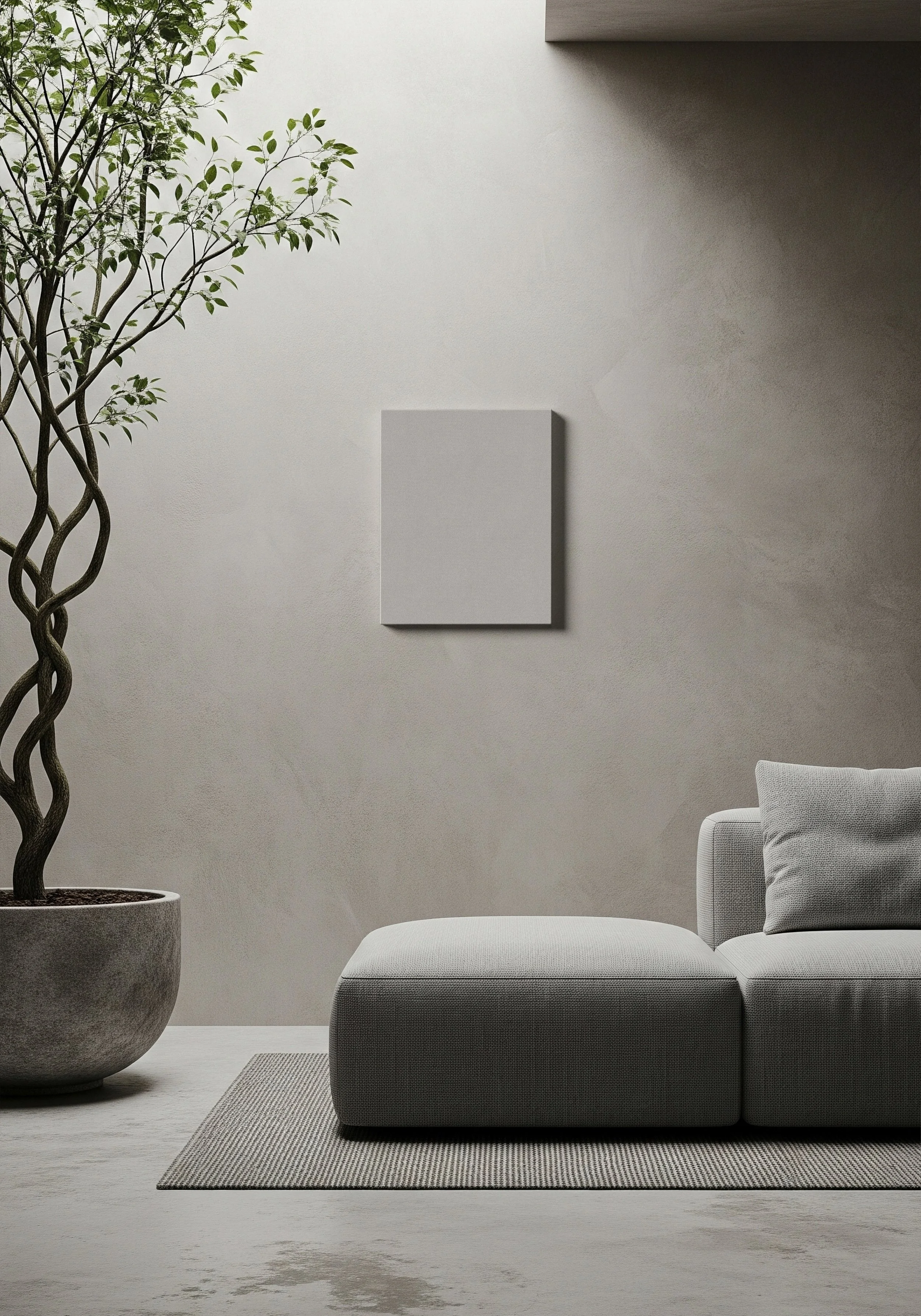 Minimalist living room with a large potted twisted tree on the left, a light gray sofa with a matching pillow, a textured rug, and a blank gray canvas on a beige wall.
