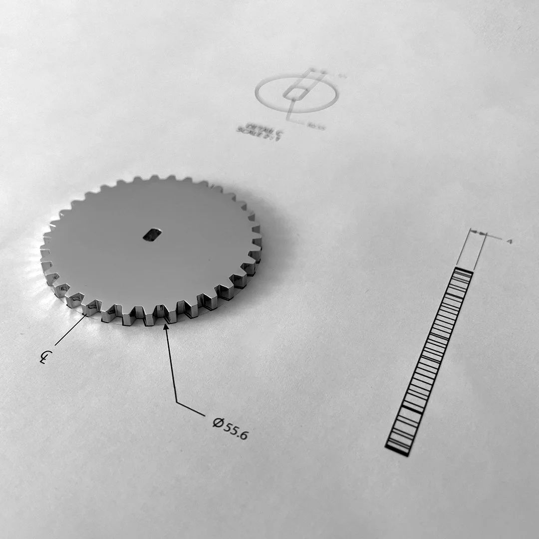 A metal gear placed on technical drawings, including a diameter measurement of 55.6 mm, and labeled with a number 3.