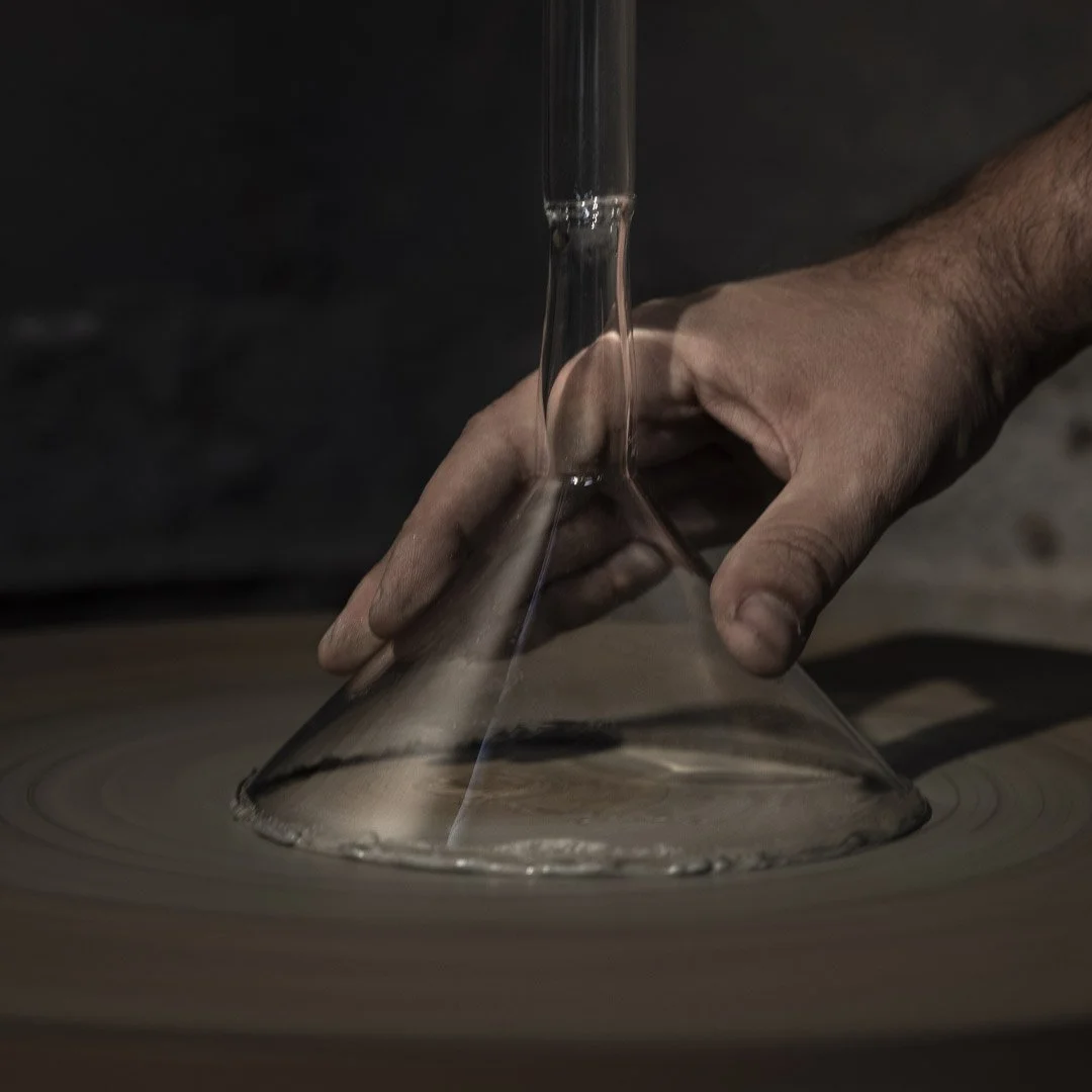 A person shaping a glass object on a rotating wheel in a glassmaking studio.