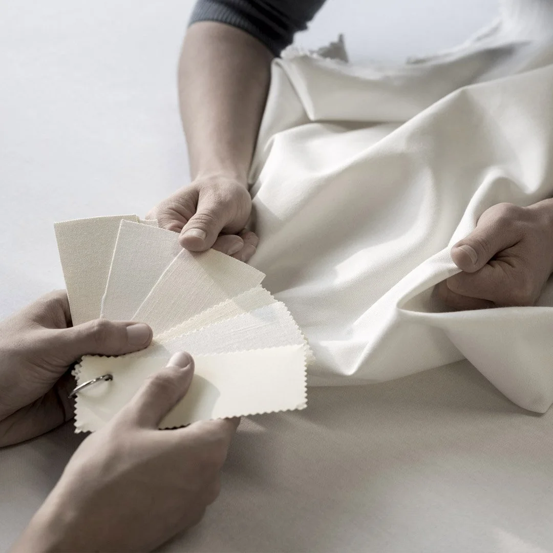 Person holding fabric swatches next to a piece of off-white or cream-colored fabric