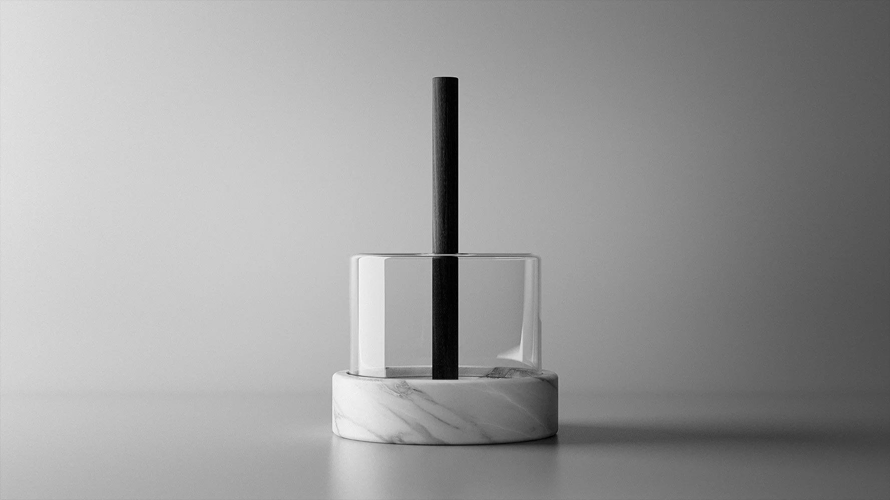 A black stick in a clear glass container with a white marble base and a rectangular marble support, set against a gray background.