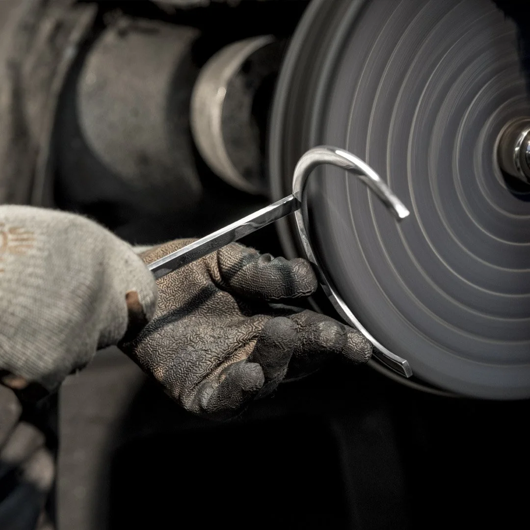 Person wearing work gloves using a sharpening tool on a circular grinding wheel.