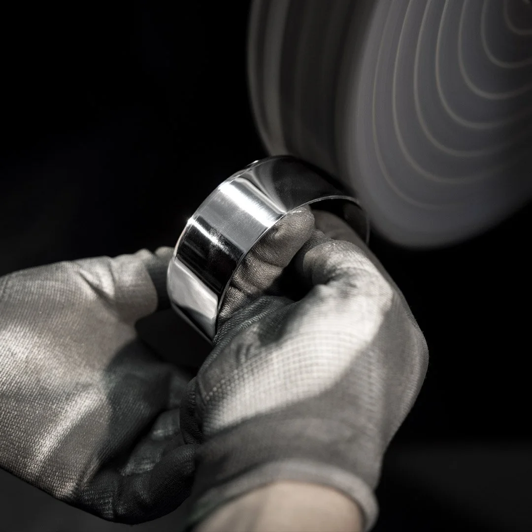 Close-up of a gloved hand polishing a shiny metal ring on a spinning lathe or polishing wheel.