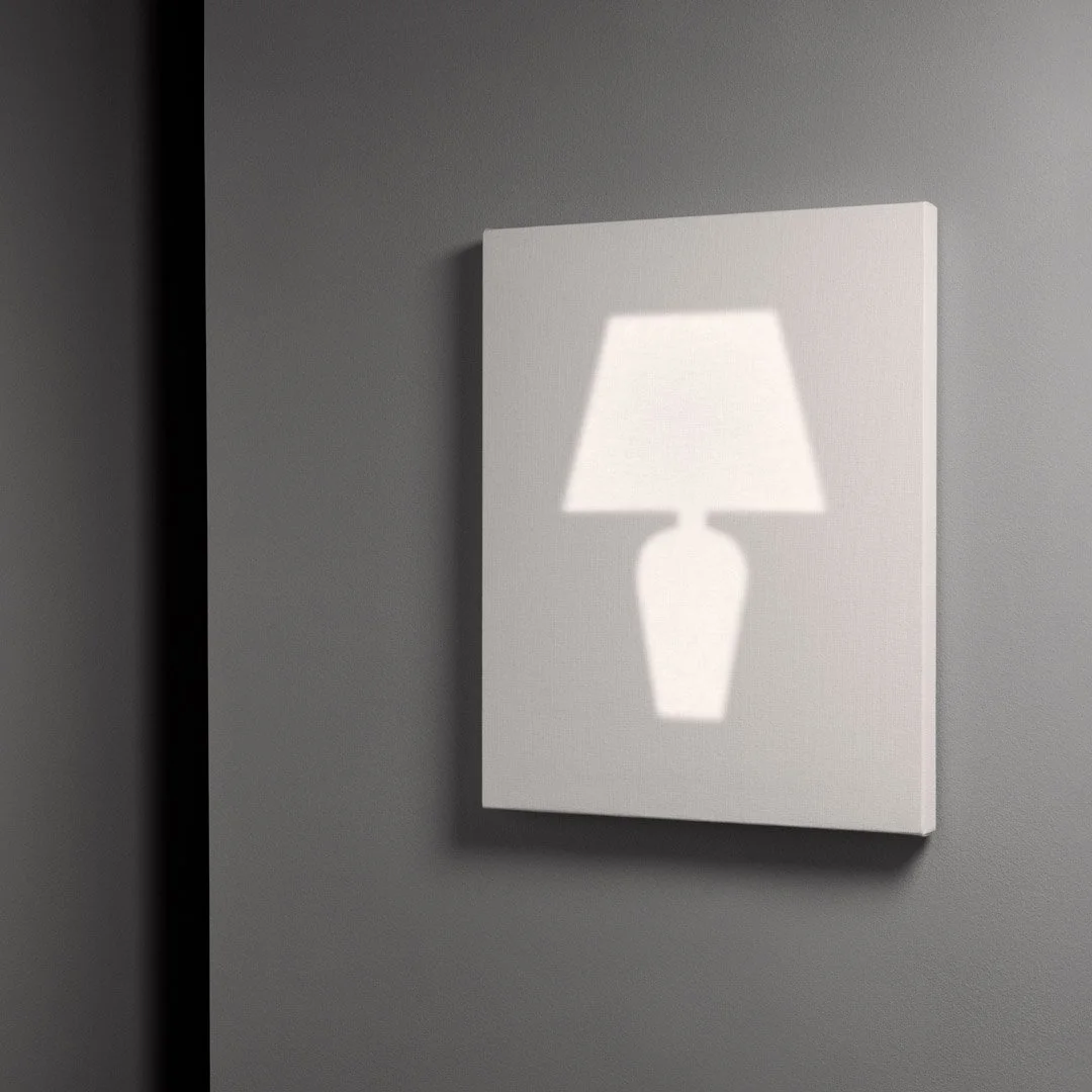 A white lampshade shadow cast on a rectangular white canvas on a gray wall.