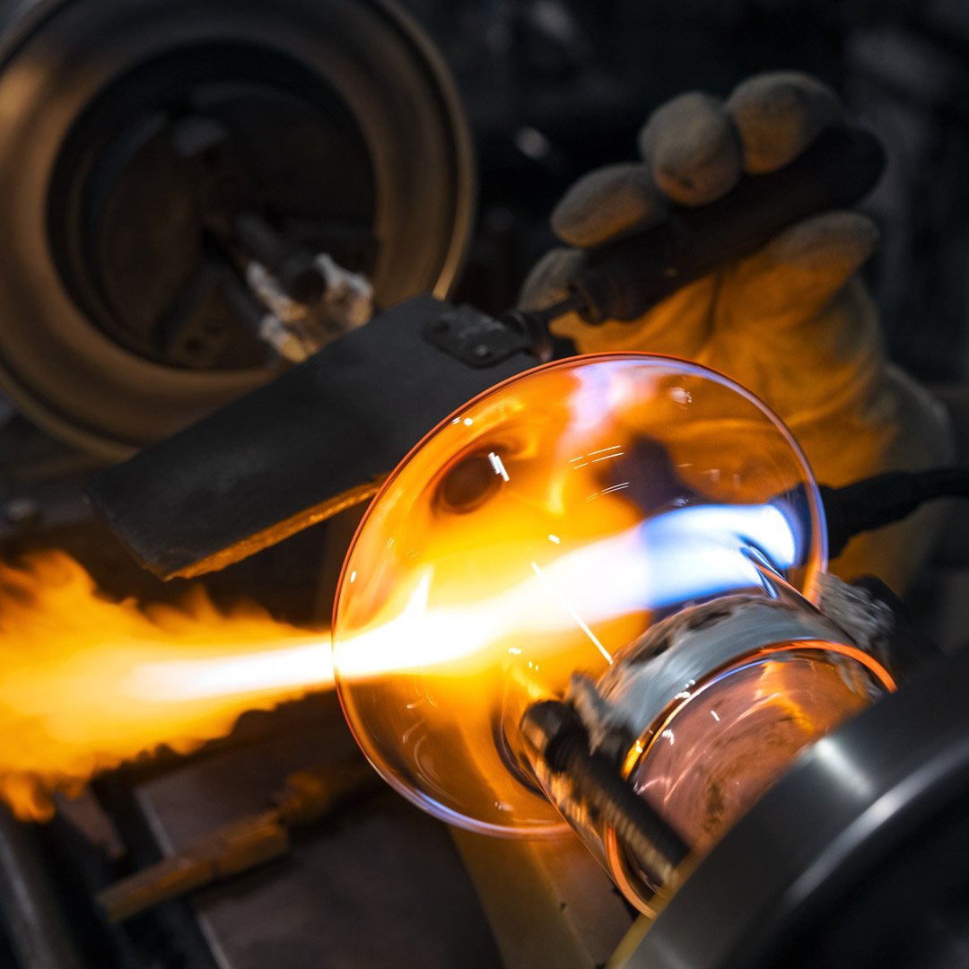 A glassblowing process creating a glass object with intense flames and glowing hot glass in a workshop setting.