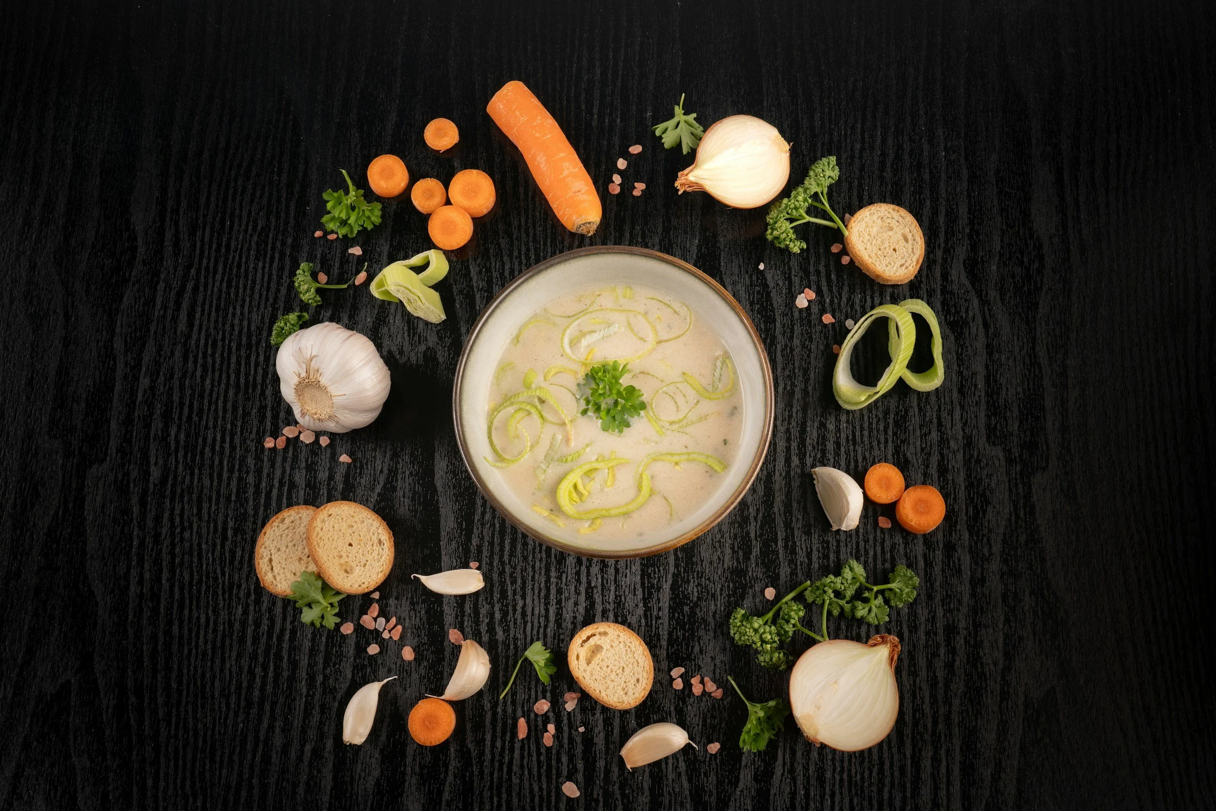 Creamy leek and potato soup with sliced leeks and vegetables on a dark wooden table