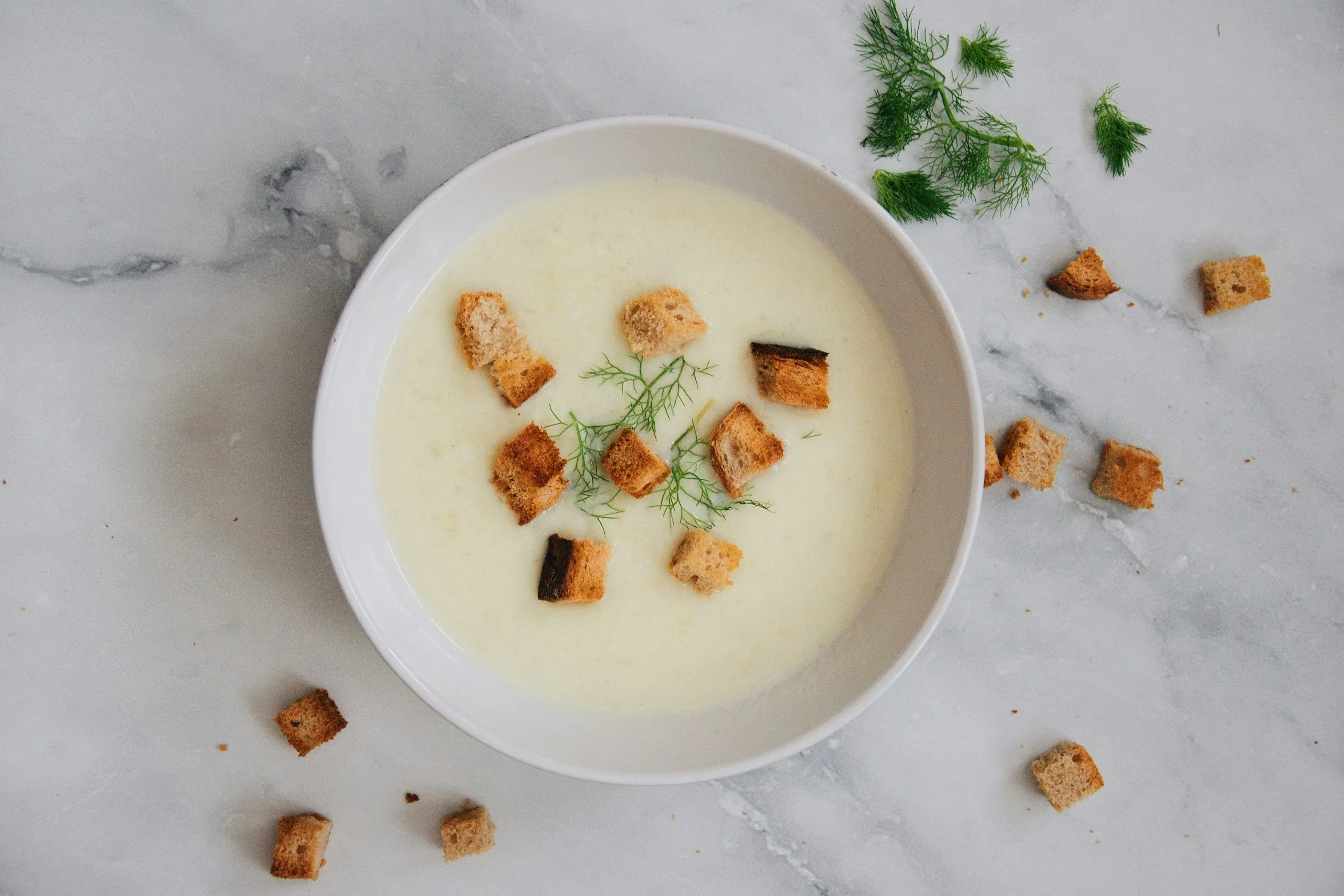 A bowl of pale creamy soup topped with golden croutons and green herbs