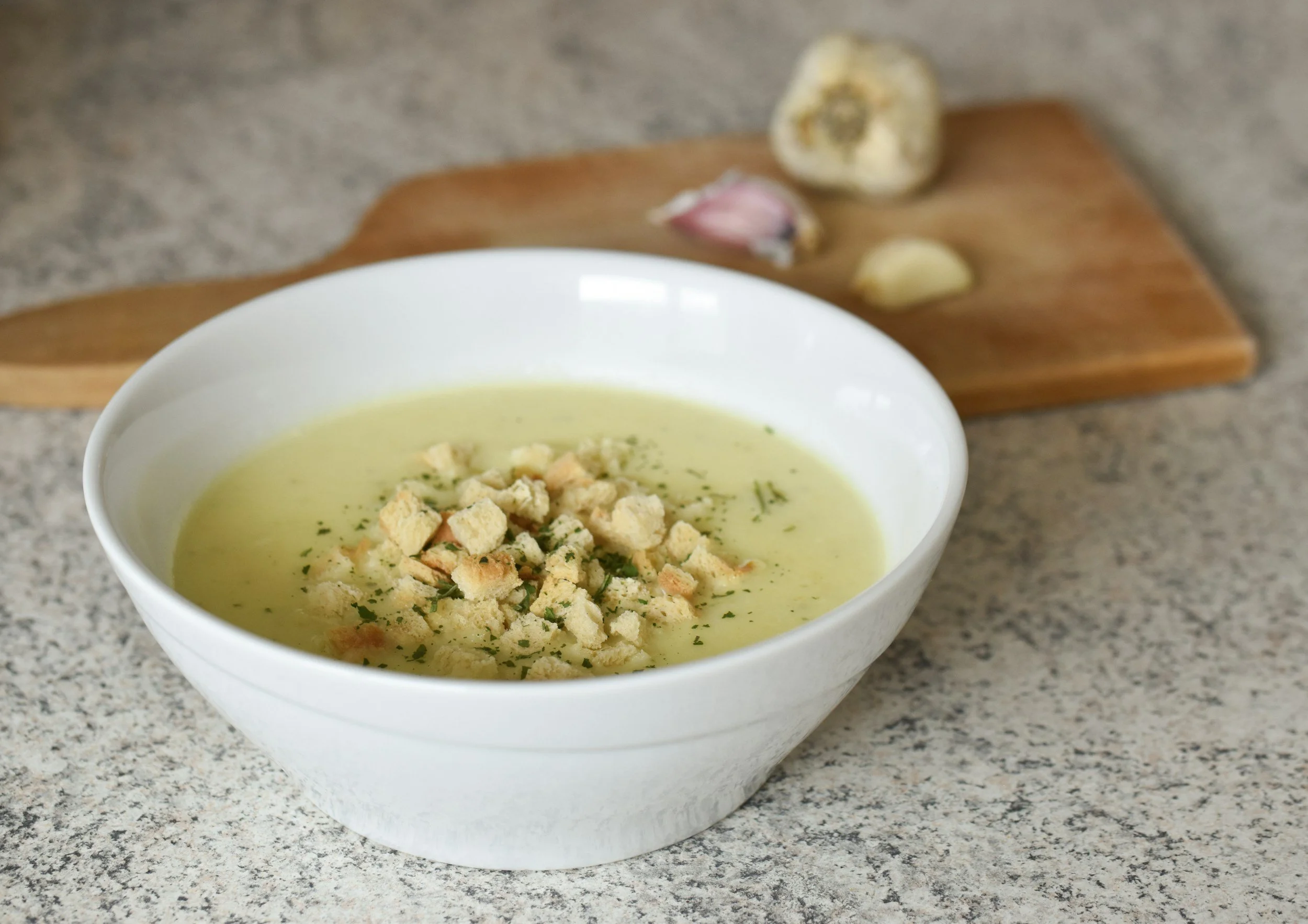Creamy cauliflower soup in a white bowl topped with small cauliflower pieces and herbs