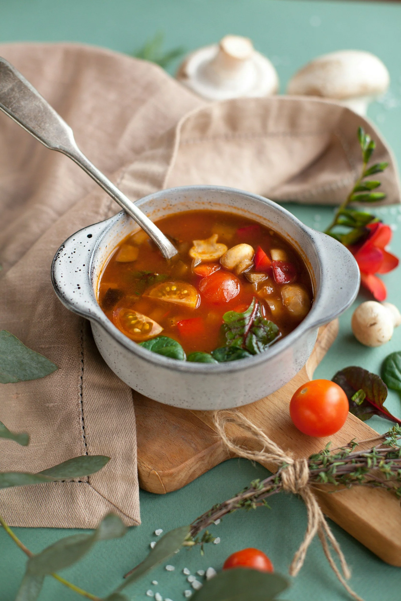 Chunky vegetable soup with red broth, peppers and green herbs in a rustic bowl