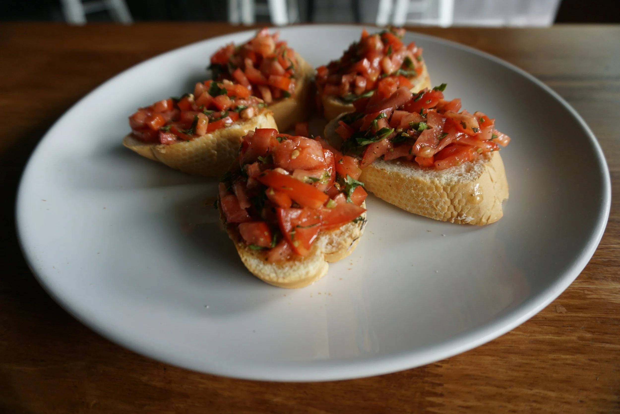 Toasted bread slices topped with chopped ripe tomatoes and fresh herbs on a white plate