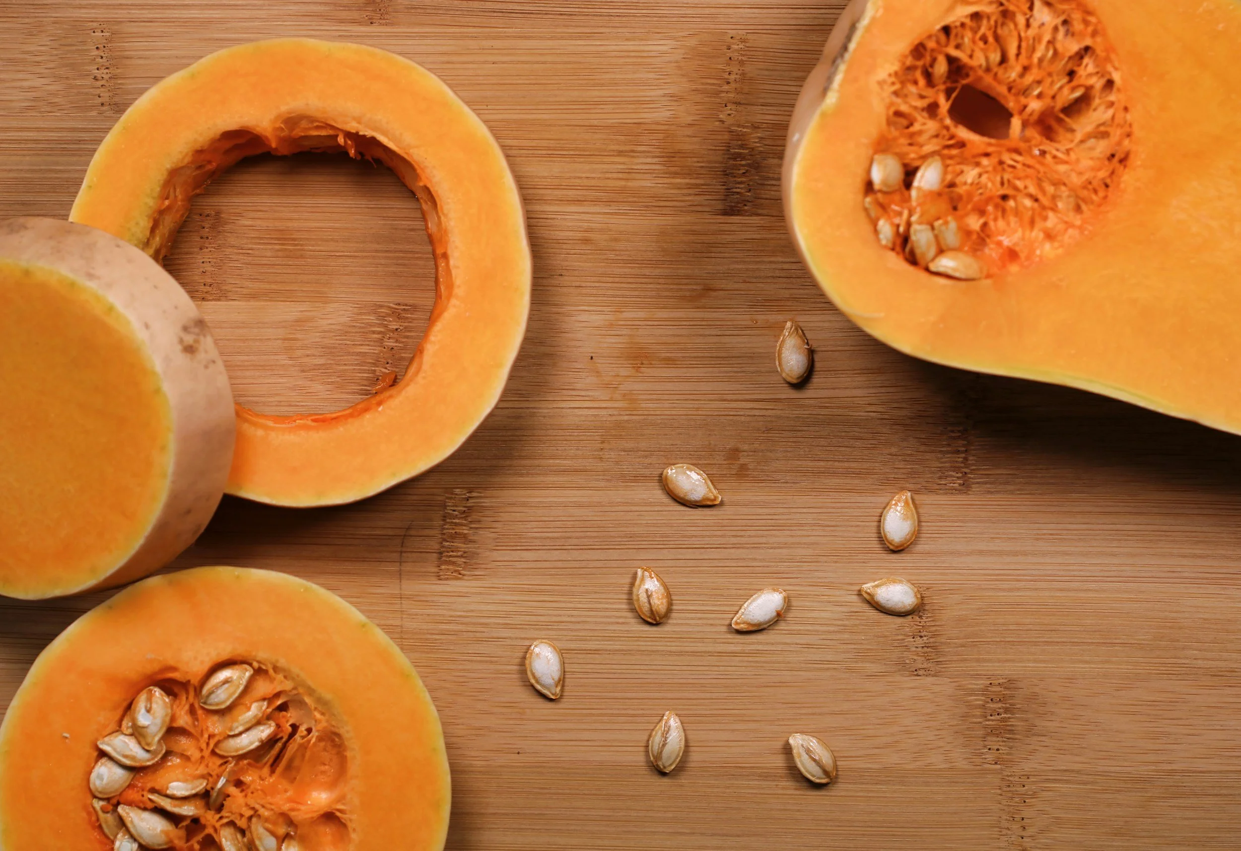 Butternut squash cut into thick slices on a wooden board with loose seeds