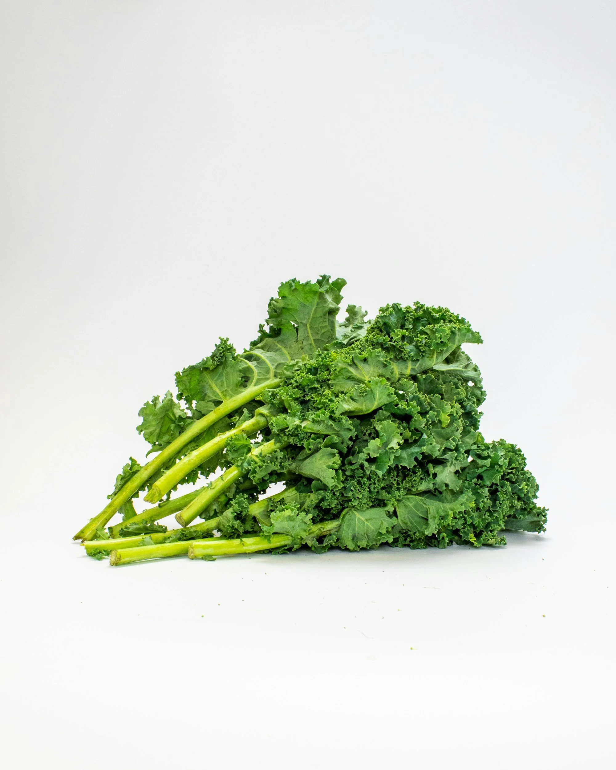 A bunch of fresh curly kale leaves on a pale background