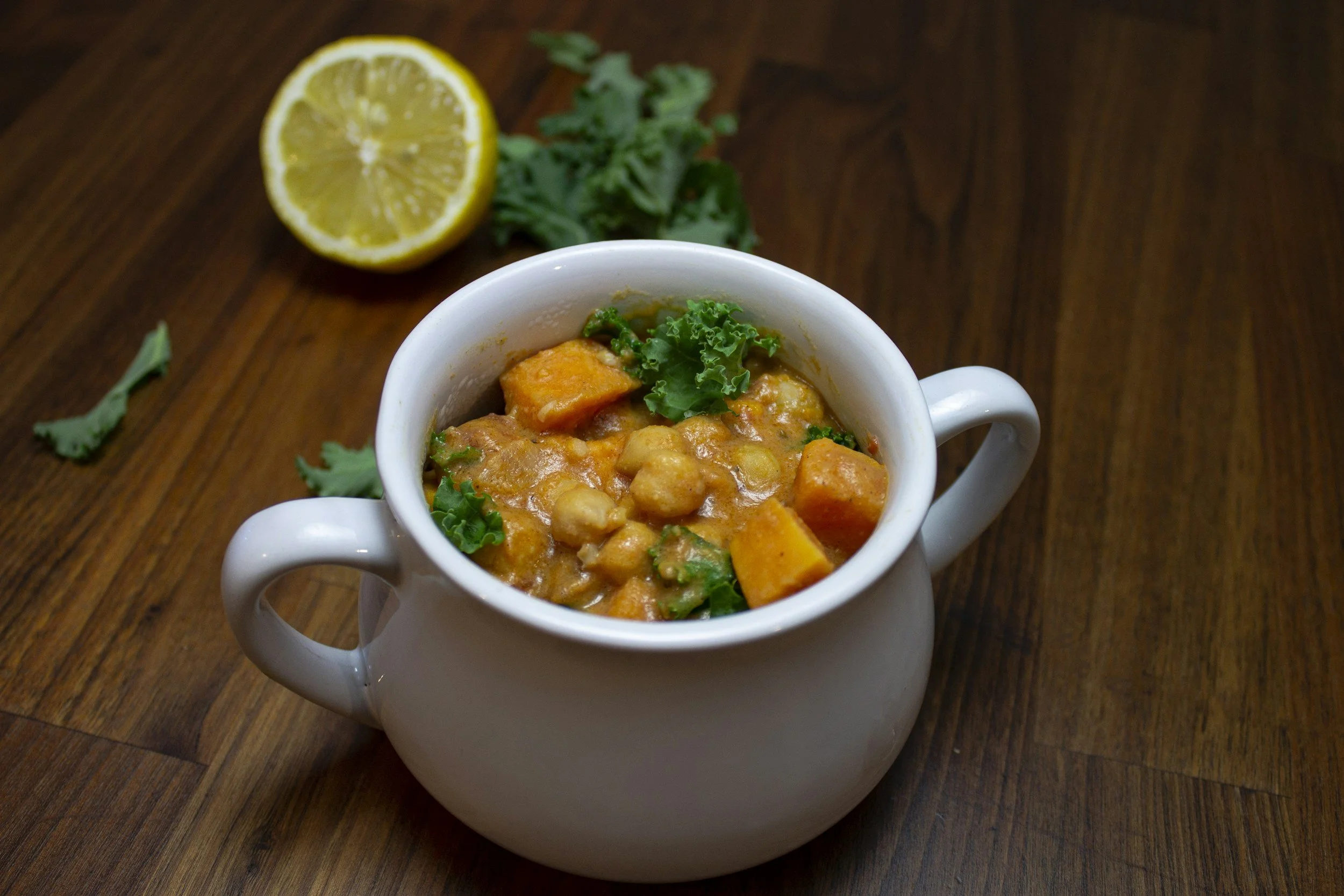 A bowl of chunky golden pumpkin and chickpea curry garnished with green herbs