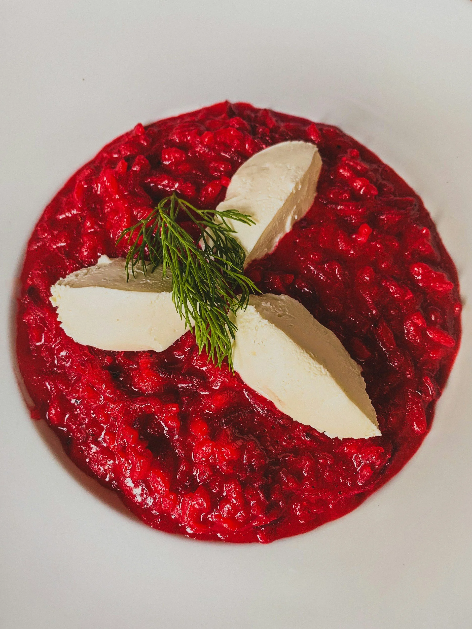 Vivid red beetroot risotto topped with pale cheese slices and fresh herbs
