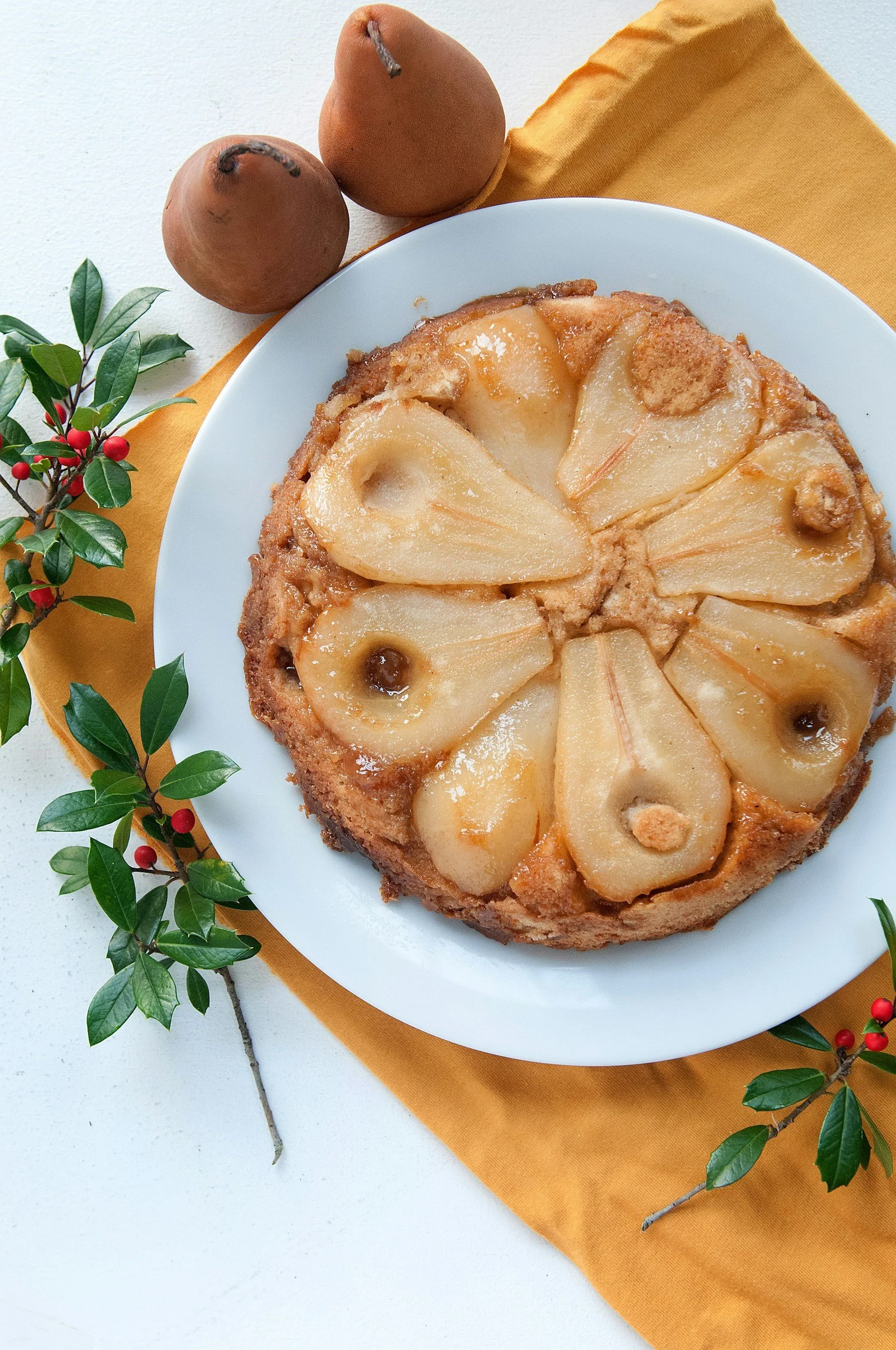 A round cake topped with a pattern of baked pear halves on a white plate