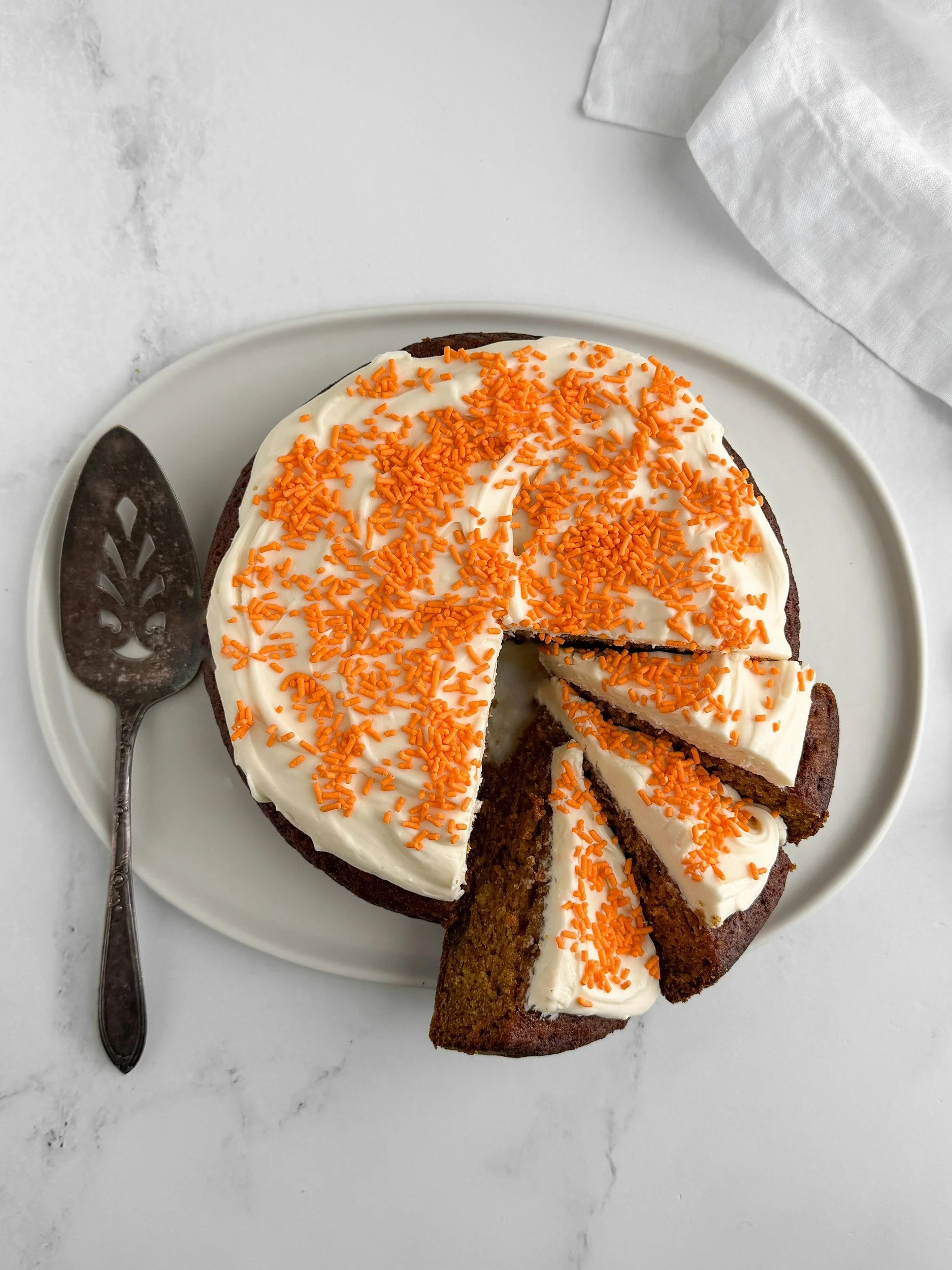 A round carrot cake with white frosting and grated carrot decoration, with slices cut out
