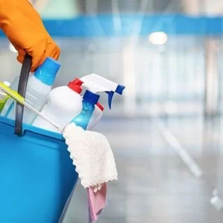 Cleaning supplies in a blue bucket, including spray bottles, a sponge, and a towel.