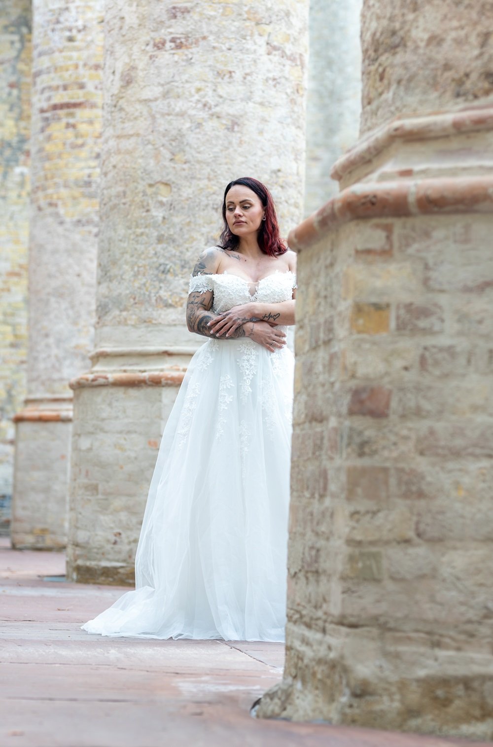 Vrouw in een witte avondjurk, zij staat tussen oude stenen zuilen, een fine art foto