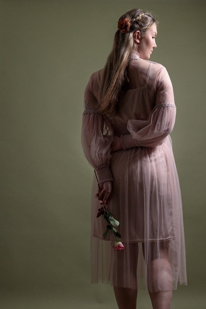 Vrouw die wegloopt in een doorzichtige roze jurk, zij houdt een roos vast, zacht, romantisch licht als een stilleven.